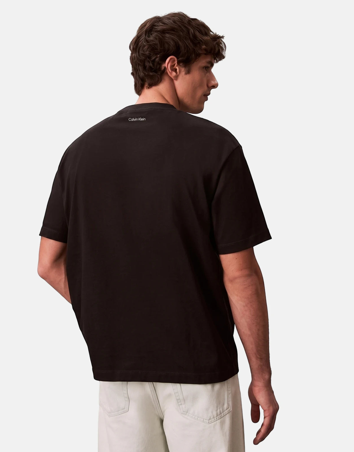 Male model wearing a black Calvin Klein 16s April Graphic Seasonal Fashion T-Shirt, shown from the back.