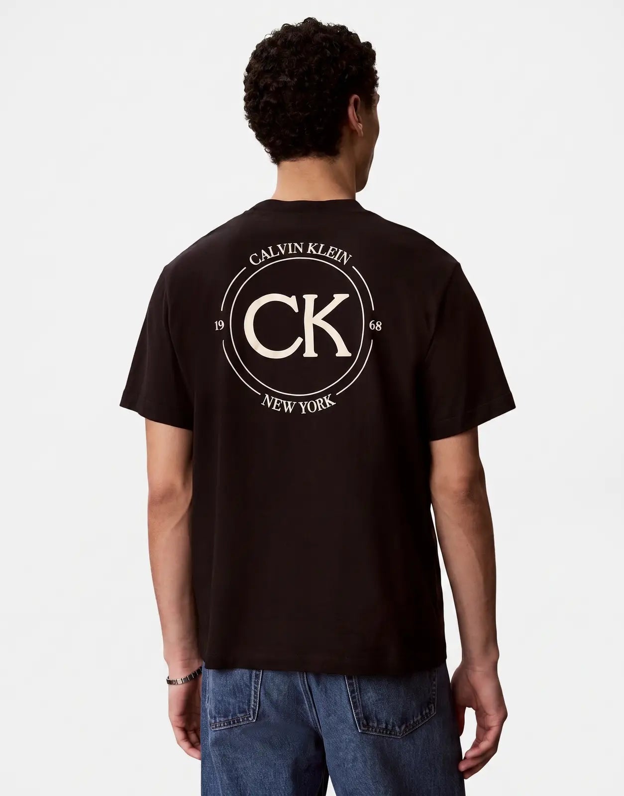 Calvin Klein 20s April Graphic Seasonal Fashion Black T-shirt with a distinctive white circular logo featuring 'CK' and 'New