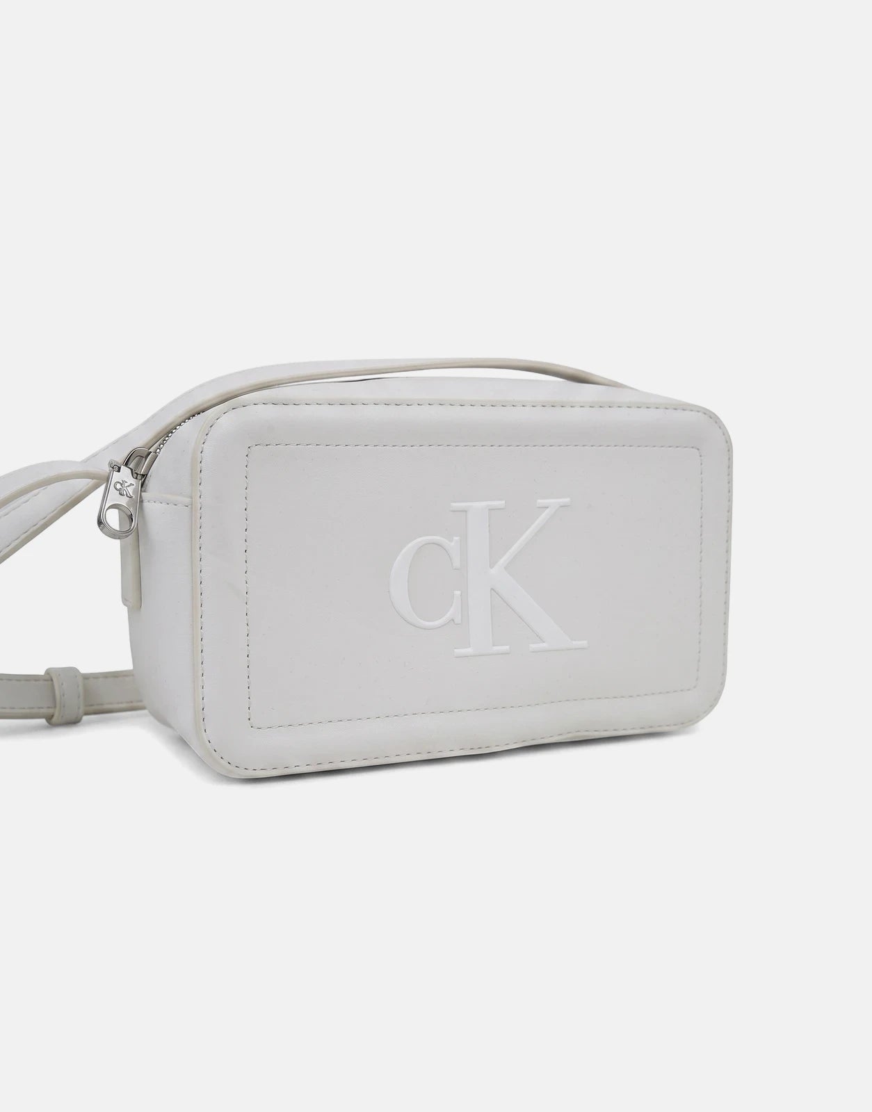 White Calvin Klein Bold CK camera bag made from a leather-like material, featuring a prominent embossed logo and silver