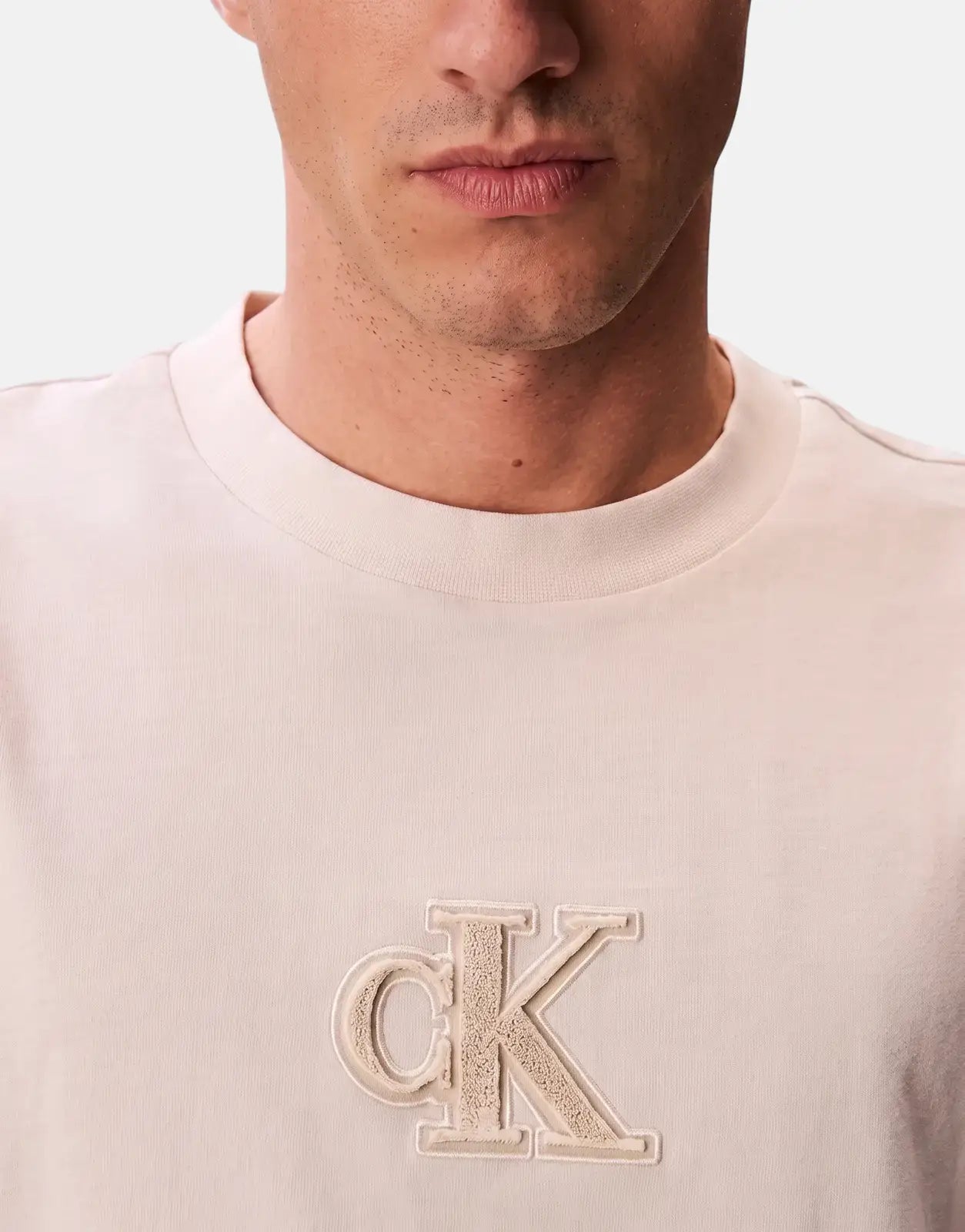 Close-up of a man wearing an off-white Calvin Klein T-shirt, featuring an embroidered CK logo on the chest.