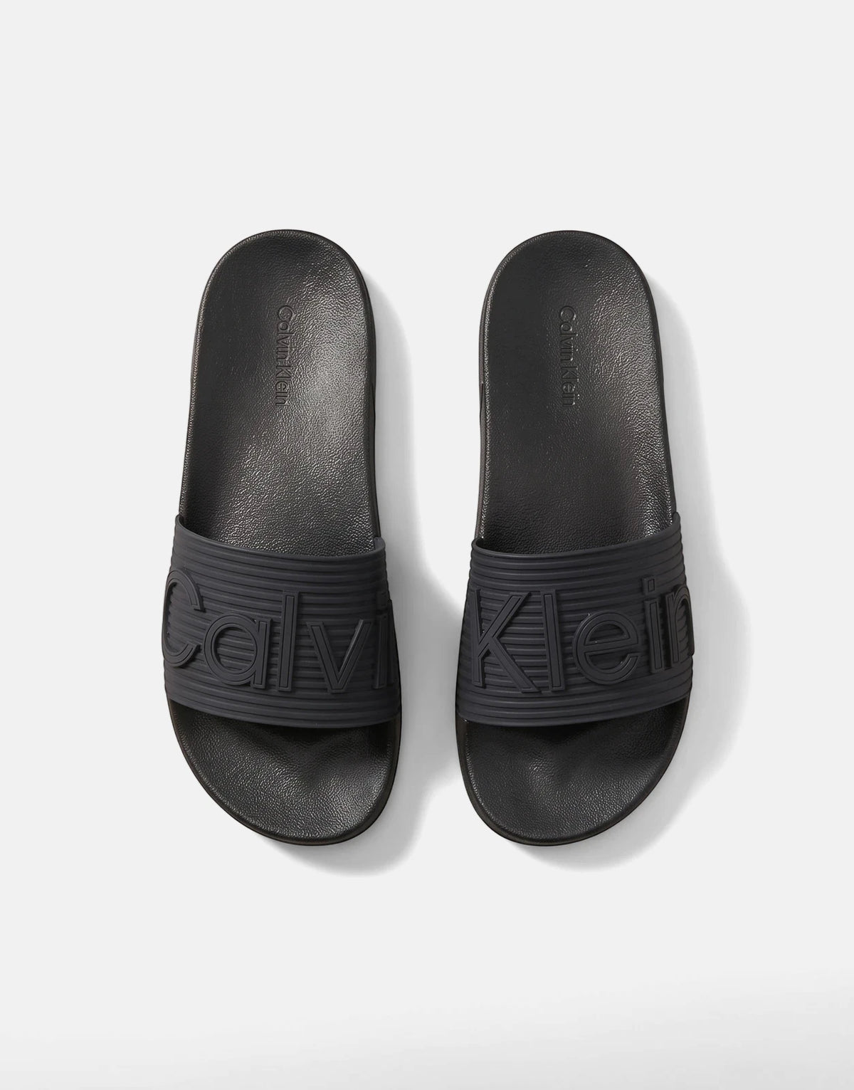 A pair of black Calvin Klein Essential Texture slides, featuring embossed branding on the strap, viewed from a top-down