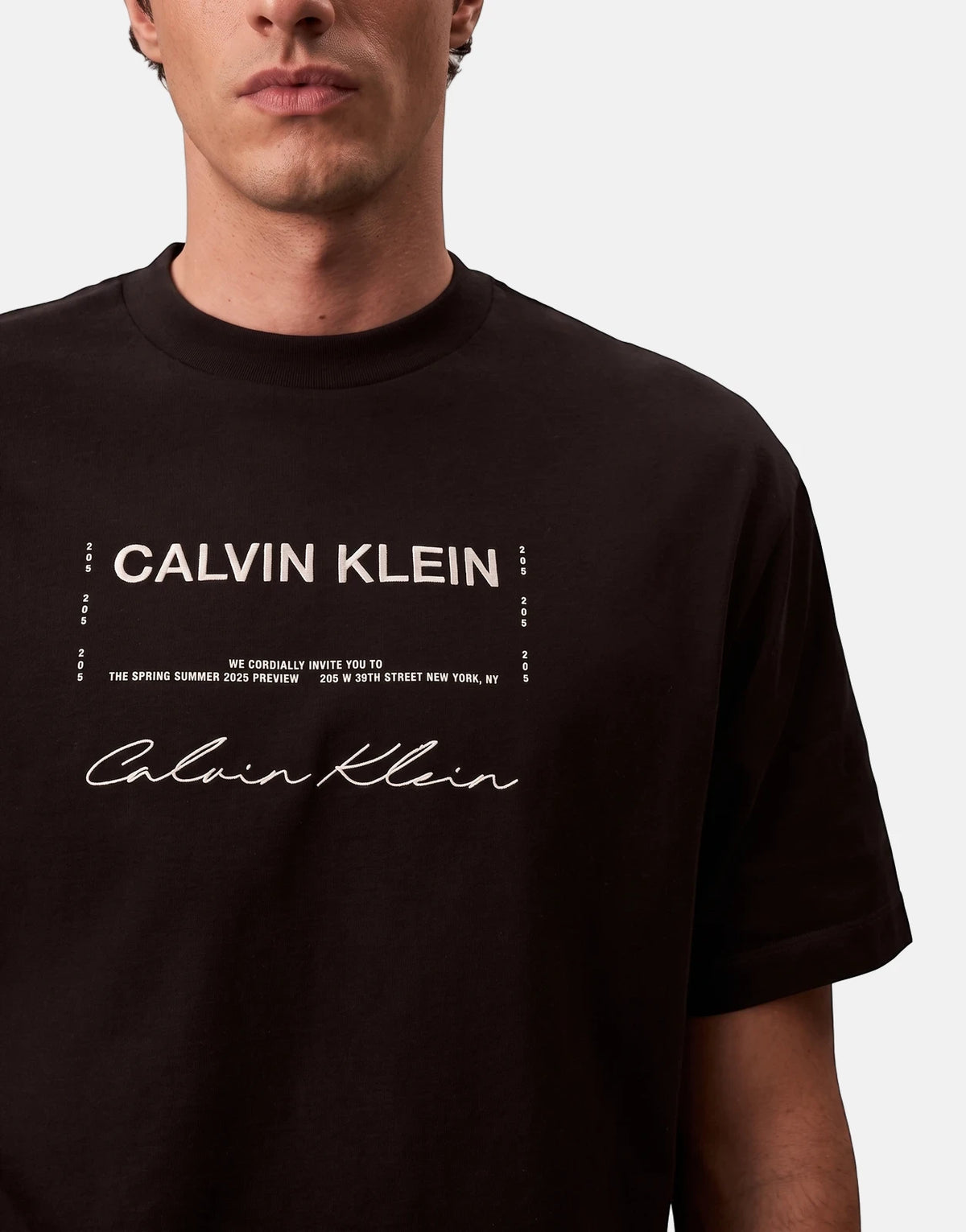 Close-up of a male model wearing a black Calvin Klein graphic t-shirt, featuring white text and logo on the chest.