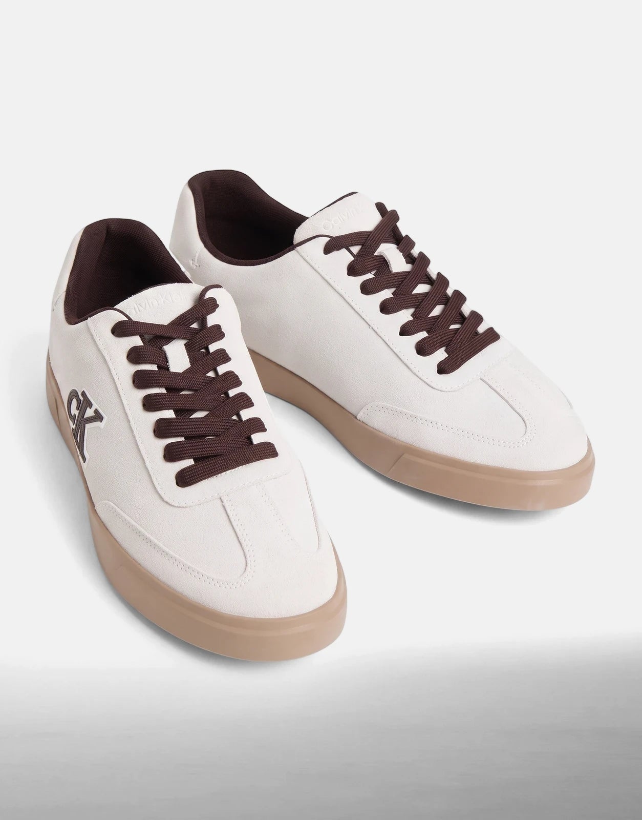 Pair of Calvin Klein Low Prof White Multi Cupsole Sneakers with brown laces and tan soles, angled view.