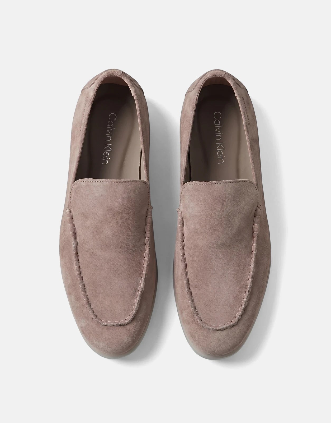 A pair of men's taupe Calvin Klein low profile loafers made of suede, with moc-toe stitching, viewed from above.