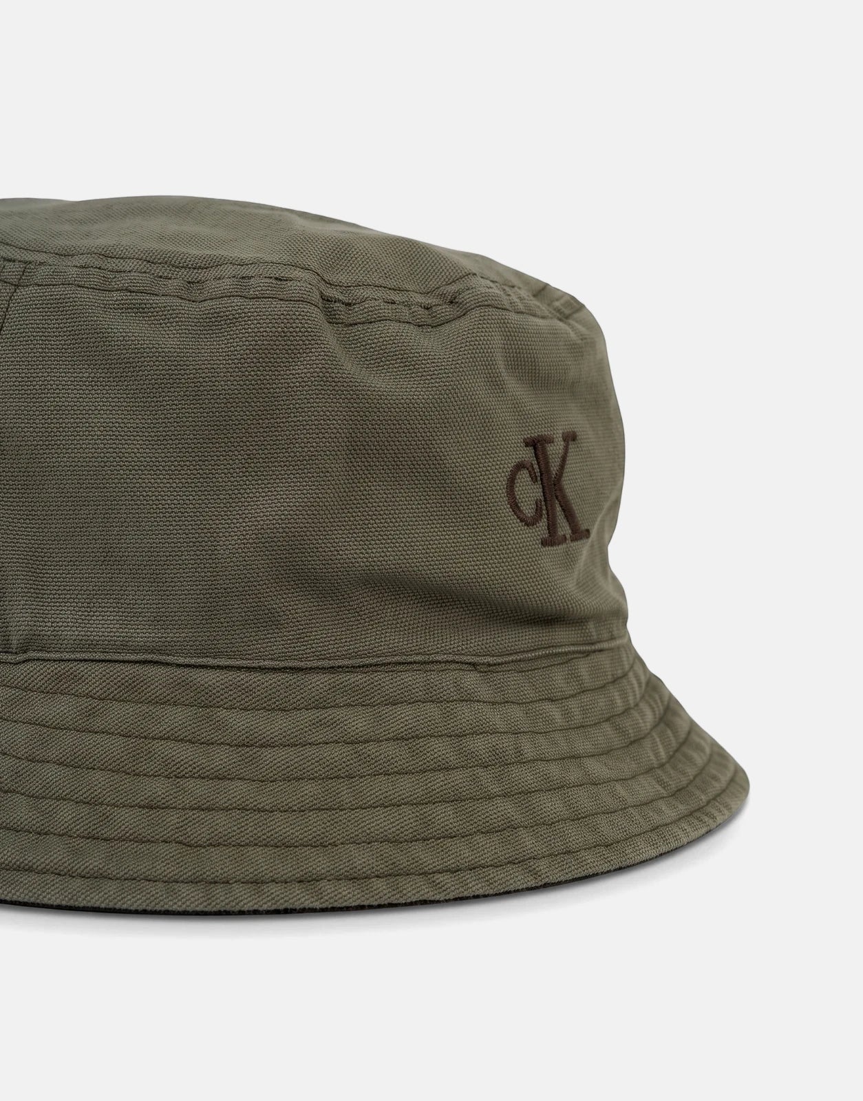 Close-up of a green Calvin Klein washed material reversible bucket hat with a brown embroidered CK logo.
