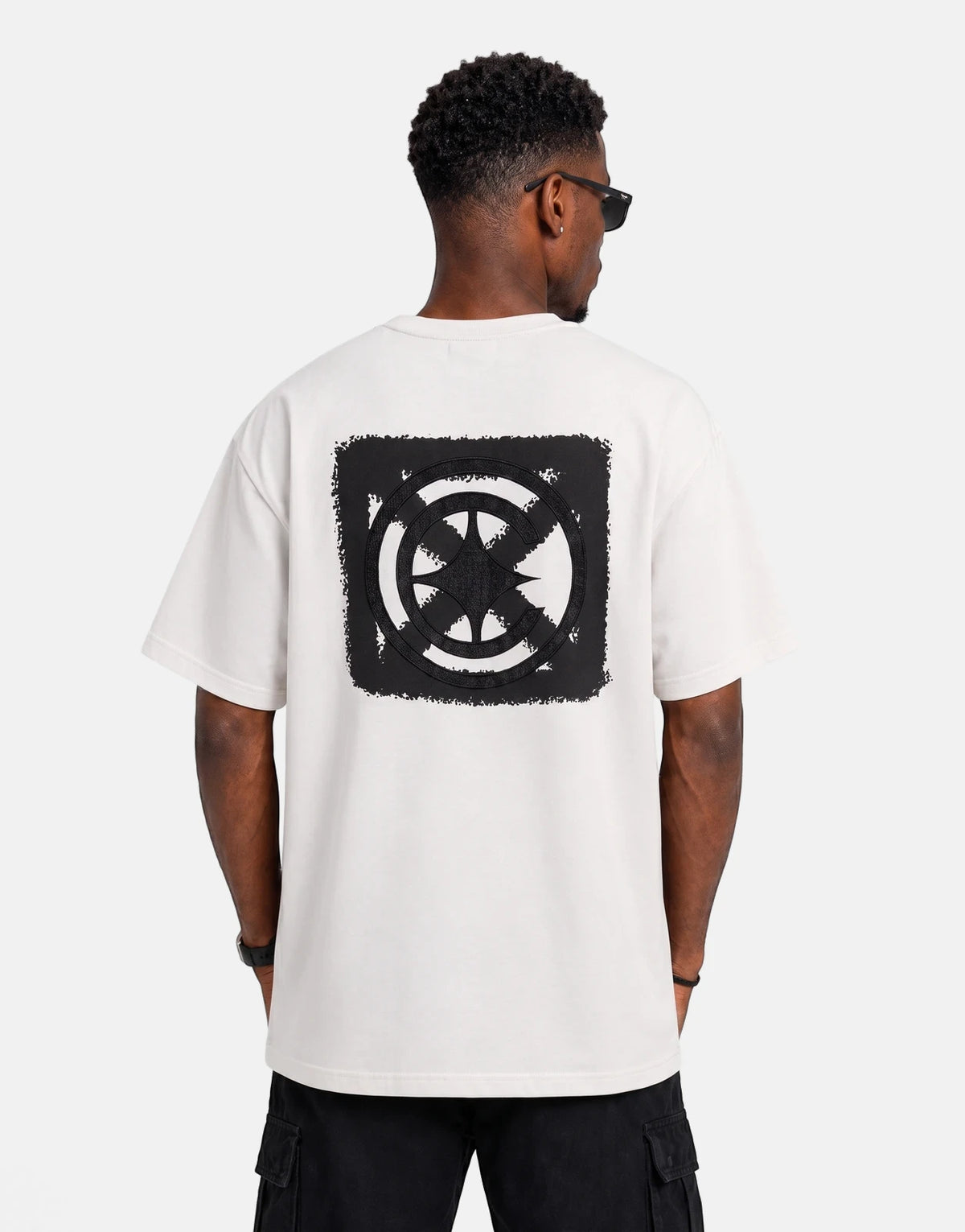 Back view of a male model wearing a Covali Denimo white oversized t-shirt with a black distressed circular graphic on the