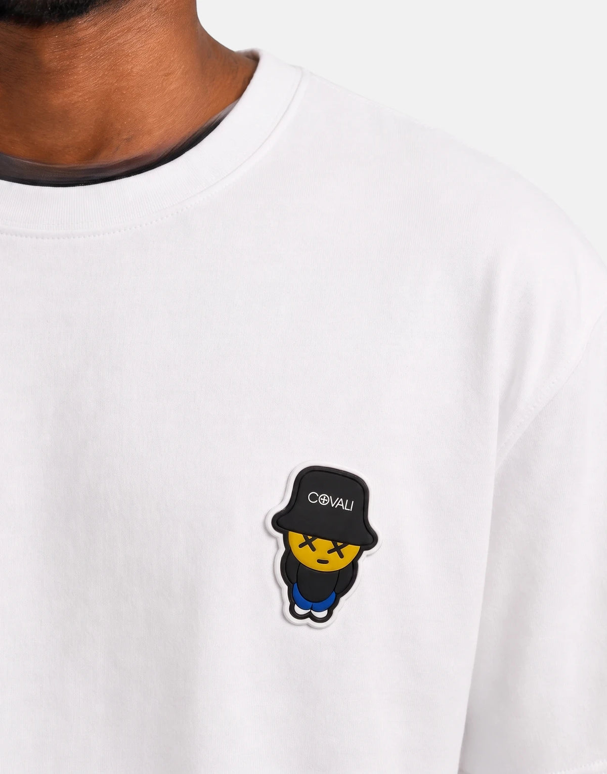 Close-up of a person wearing a white Covali Tipo T-shirt, featuring a unique yellow face with X-eyes and black bucket hat