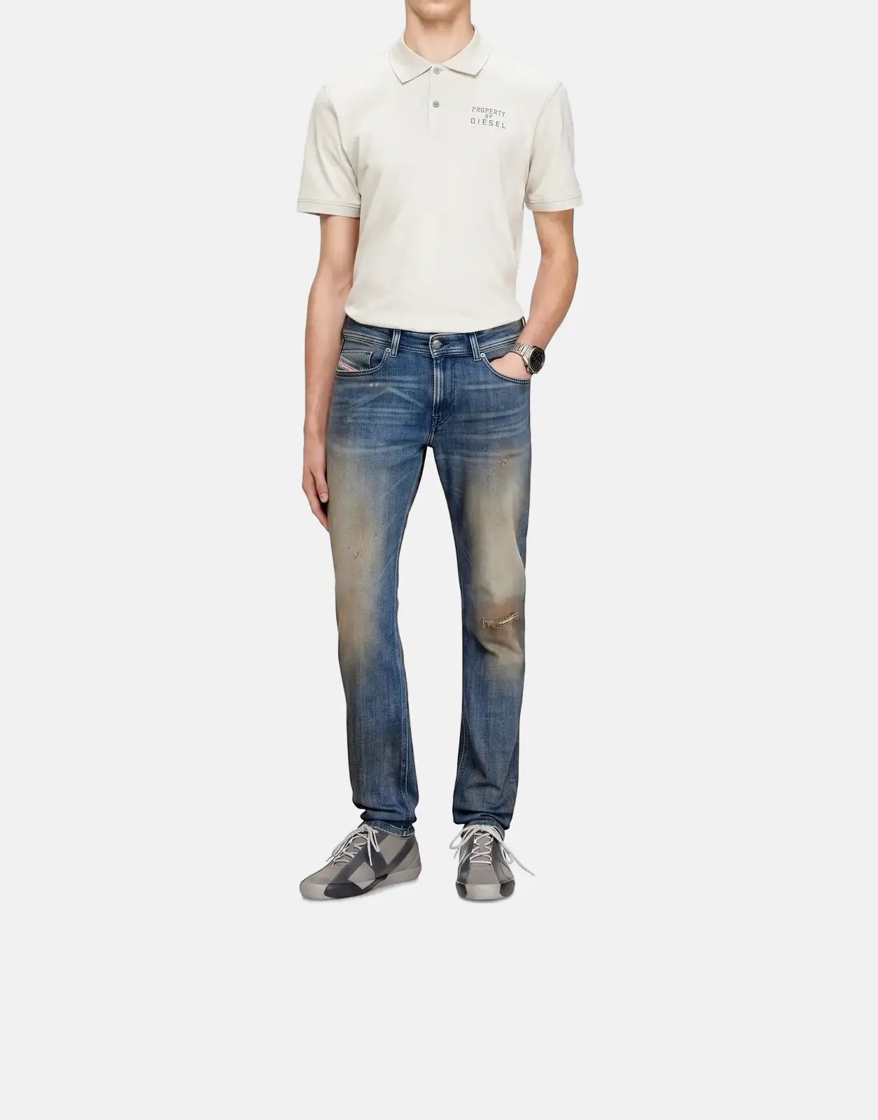 Male model wearing Diesel 1979 Sleenker skinny fit distressed blue denim jeans, a light beige polo shirt, and gray sneakers.