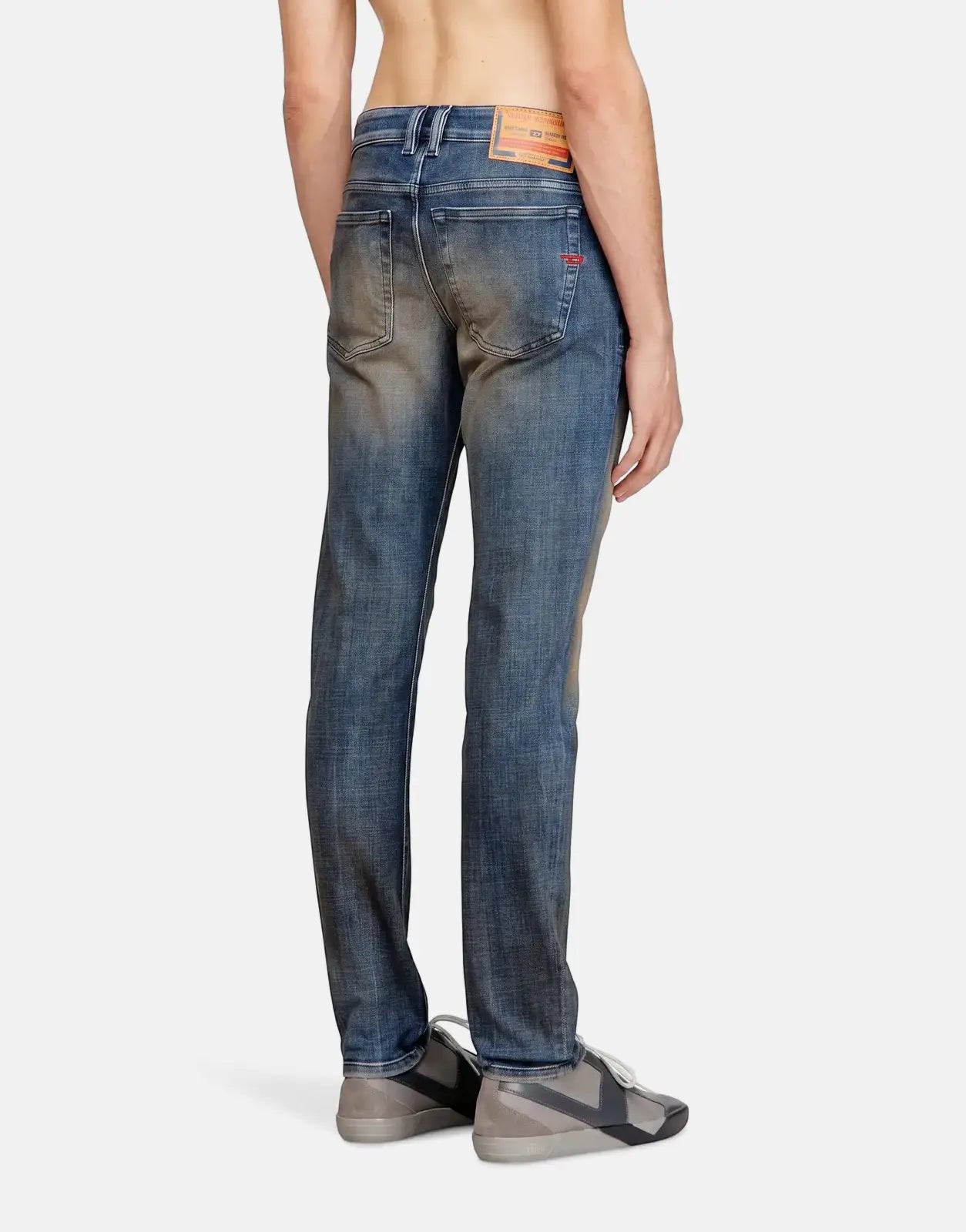 Man from behind wearing blue washed Diesel 1979 Sleenker skinny denim jeans with grey and black sneakers.