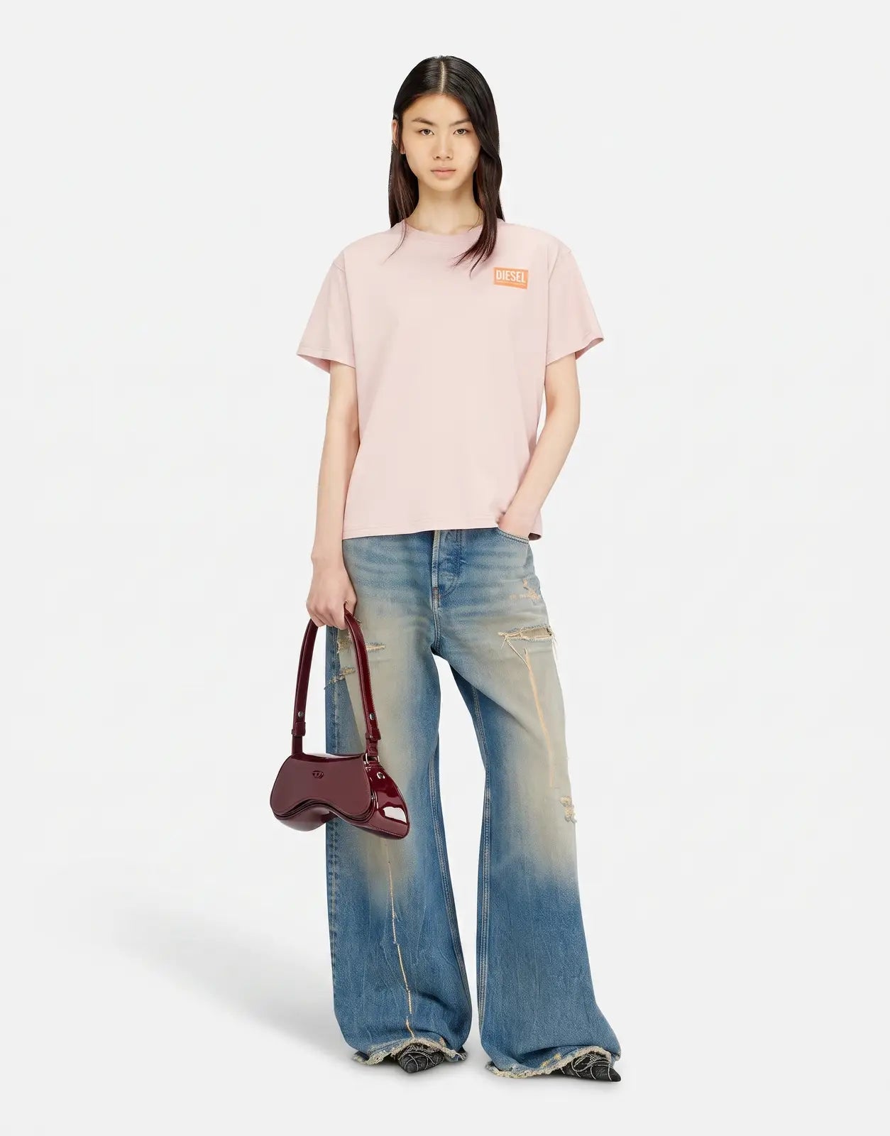 Female model wearing a light pink Diesel T-Normy S6 Regular T-Shirt, distressed wide-leg jeans, and a glossy red shoulder