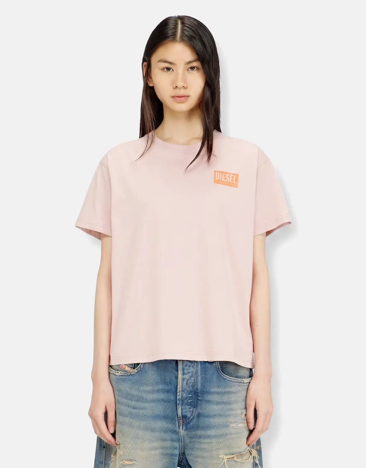 A young woman wearing a light pink Diesel T-Normy S6 Regular T-Shirt and distressed blue denim jeans, waist-up view.