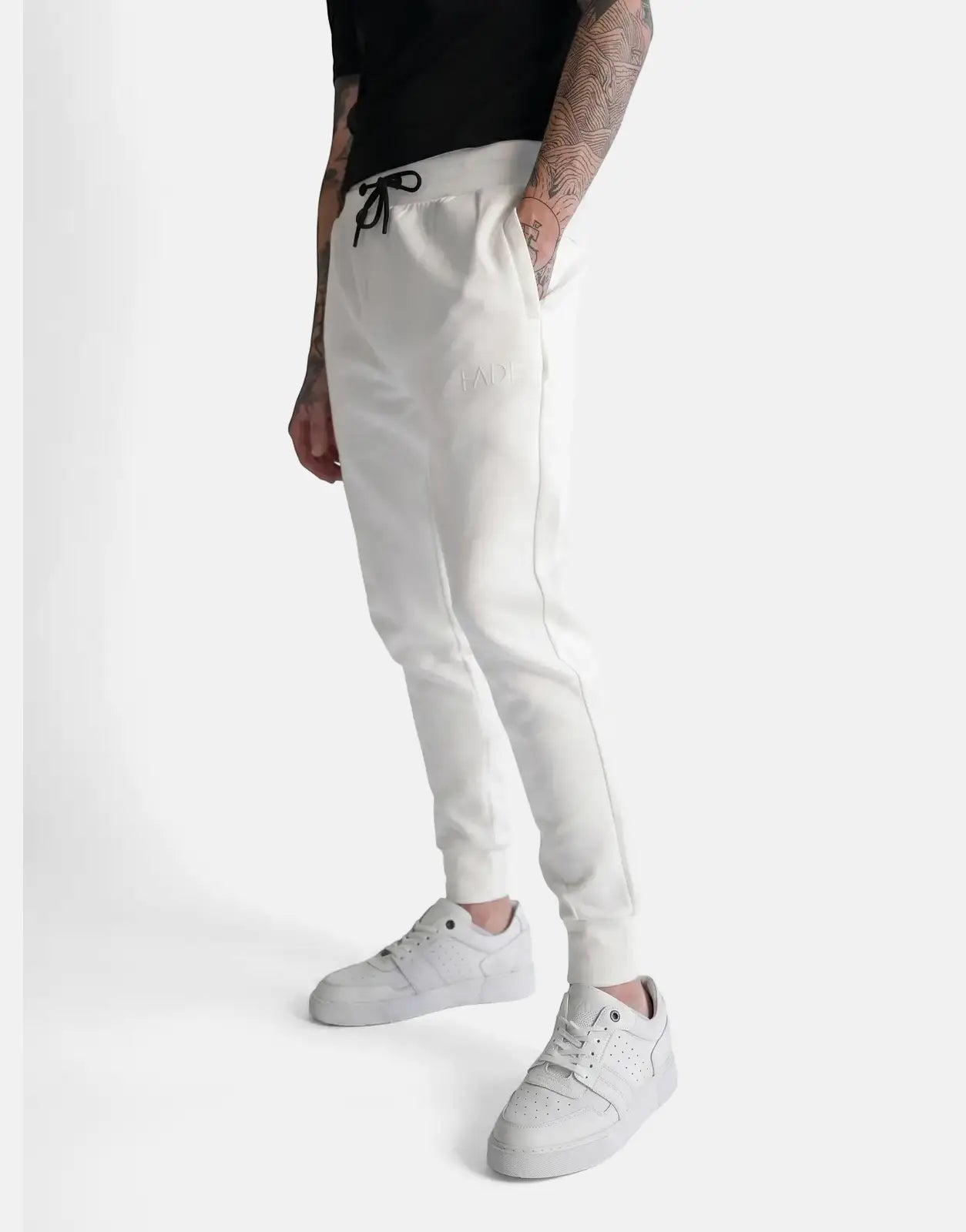 Off-white Fade Essential Sweatpants worn by a tattooed male model with a black t-shirt and white sneakers in a studio