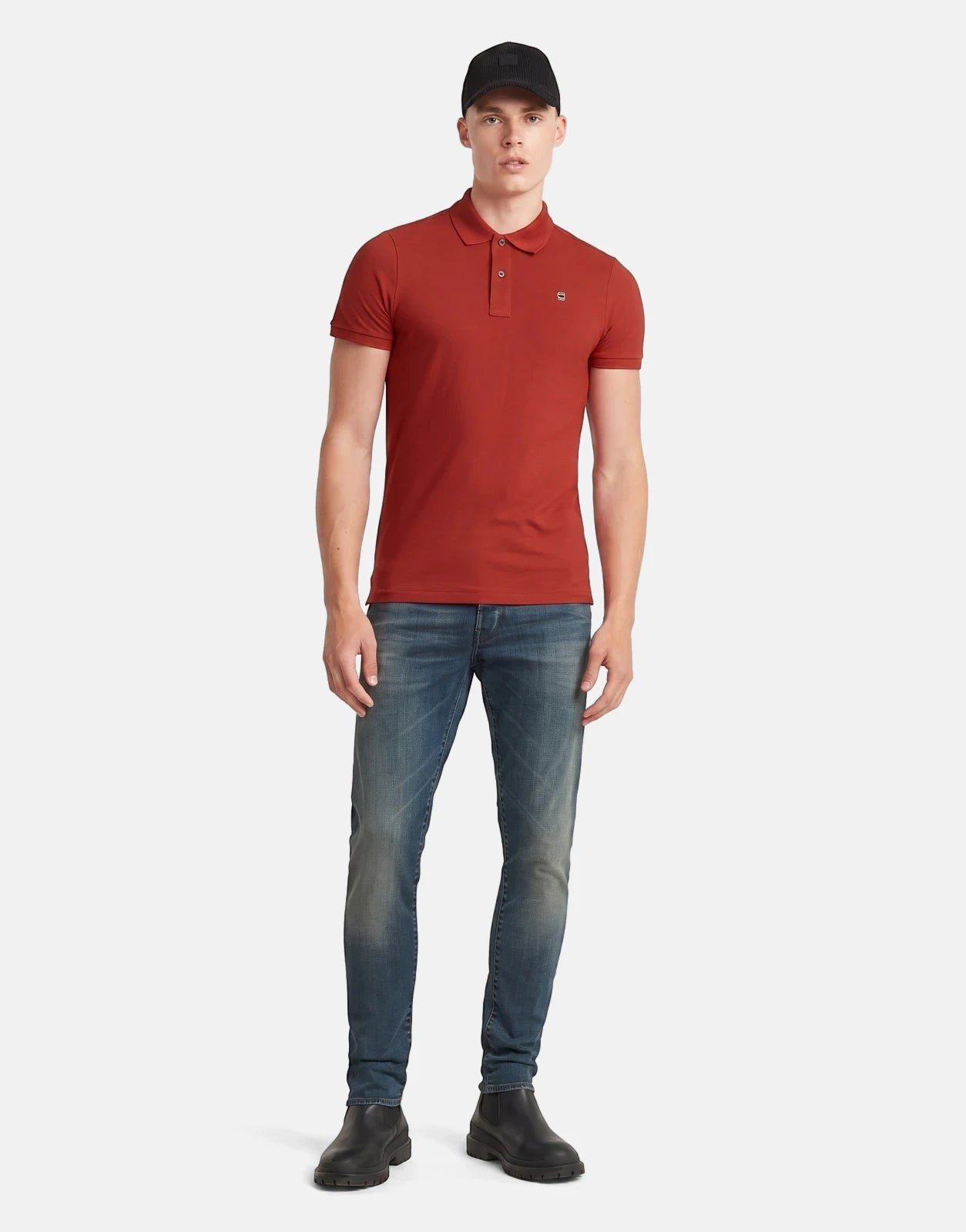 Full body shot of a male model wearing G-Star RAW 3301 Slim Faded Worker Blue Jeans, a red polo shirt, and a black cap.