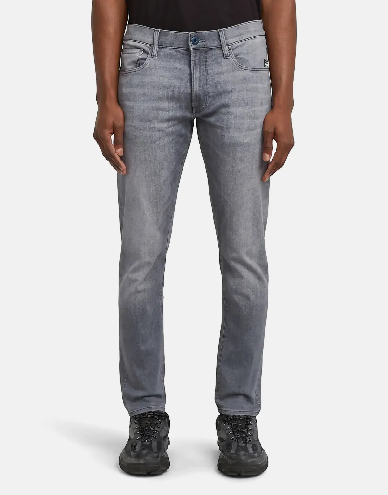 G-Star RAW 3301 Sun Faded Glacier Grey men's jeans with black sneakers on a plain background, front view.