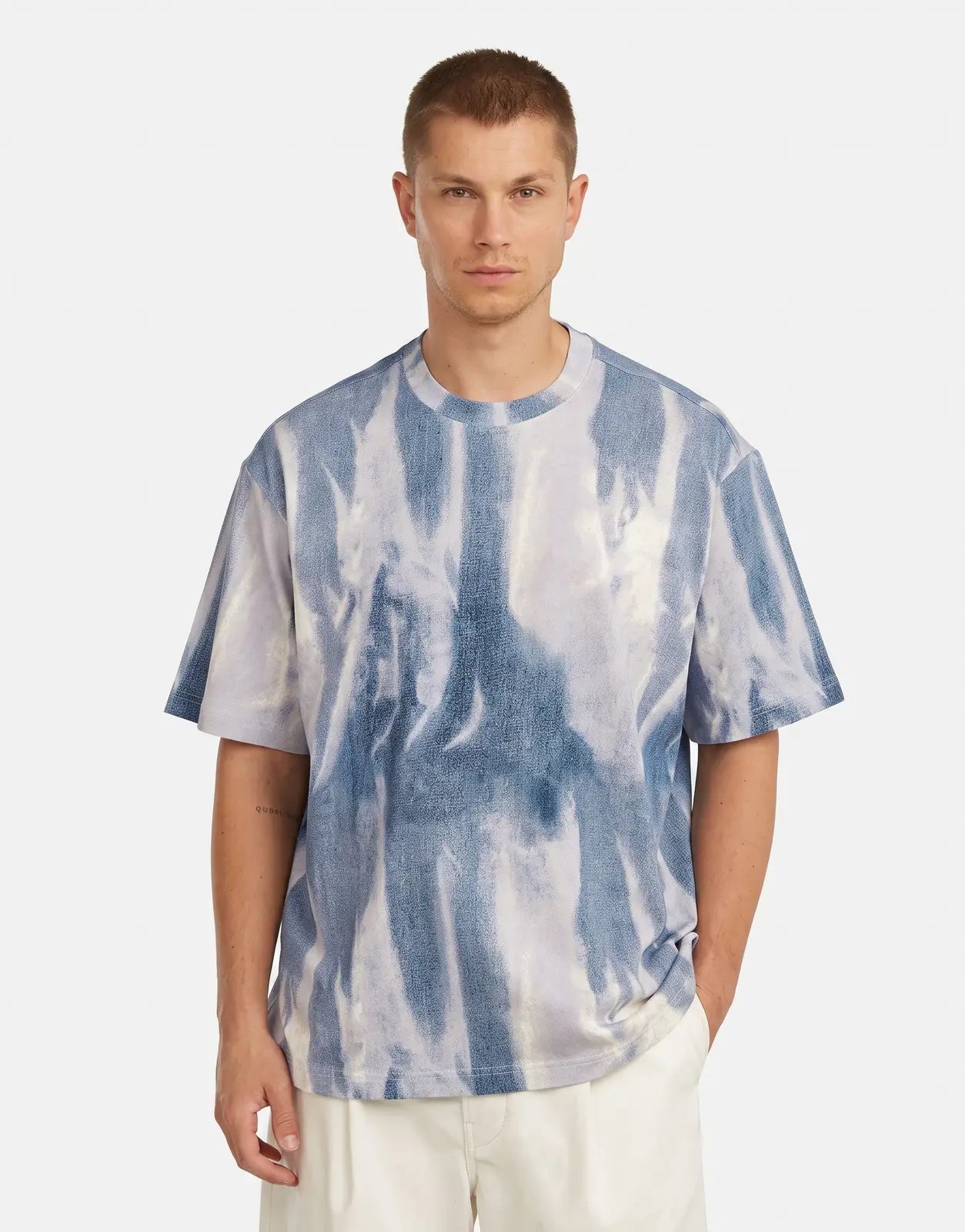 A male model wears a G-Star RAW All Over Loose Denim Flame T-Shirt, featuring a unique blue and white tie-dye pattern on its