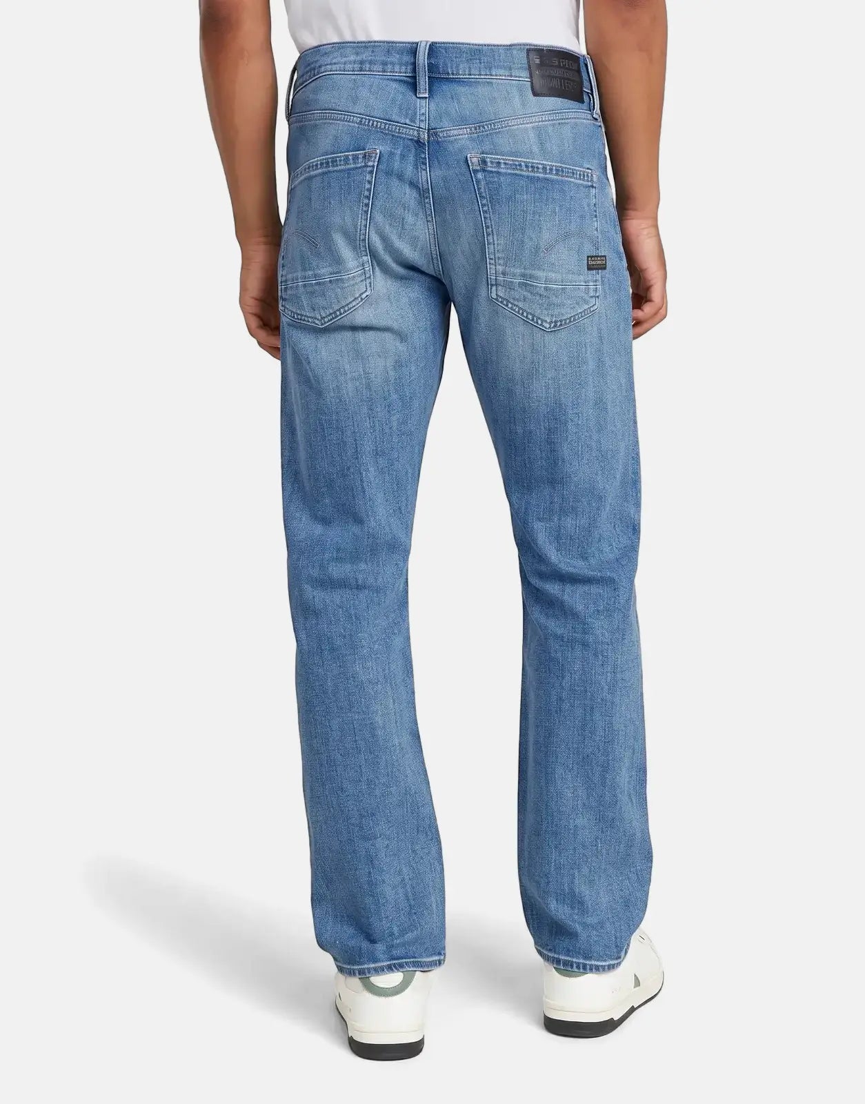 A person wears G-Star RAW Dakota Regular Faded Niagara Jeans, visible from behind, showcasing the blue faded denim with back