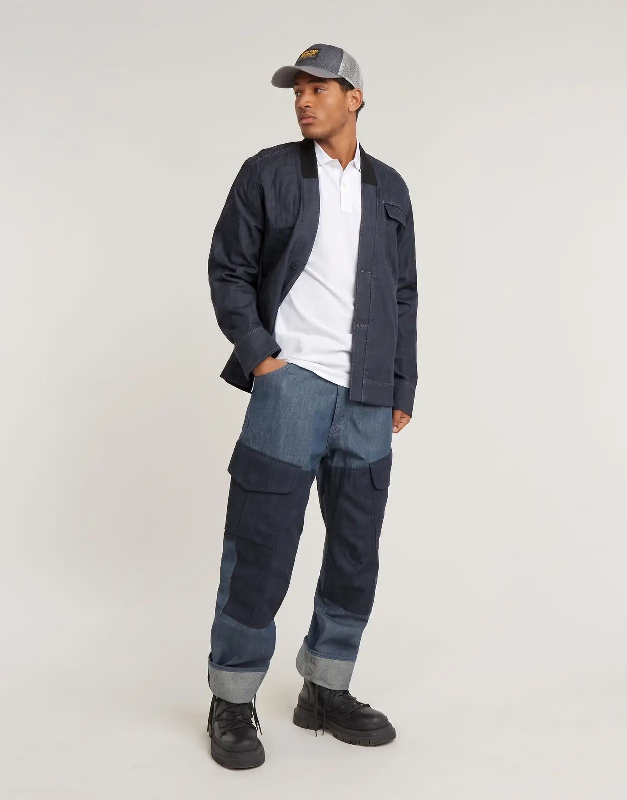 G-Star RAW Dunda Slim Stripe White Polo Shirt on a male model, styled with a dark denim jacket, patchwork jeans, and a cap.
