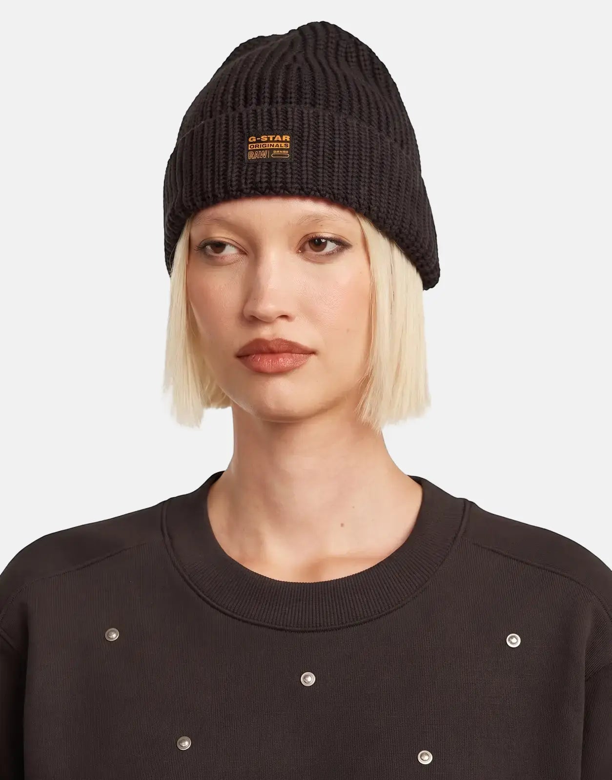 G-Star RAW Originals Fisherman Ganache Beanie, black knit, worn by a woman with a black silver-studded sweatshirt.