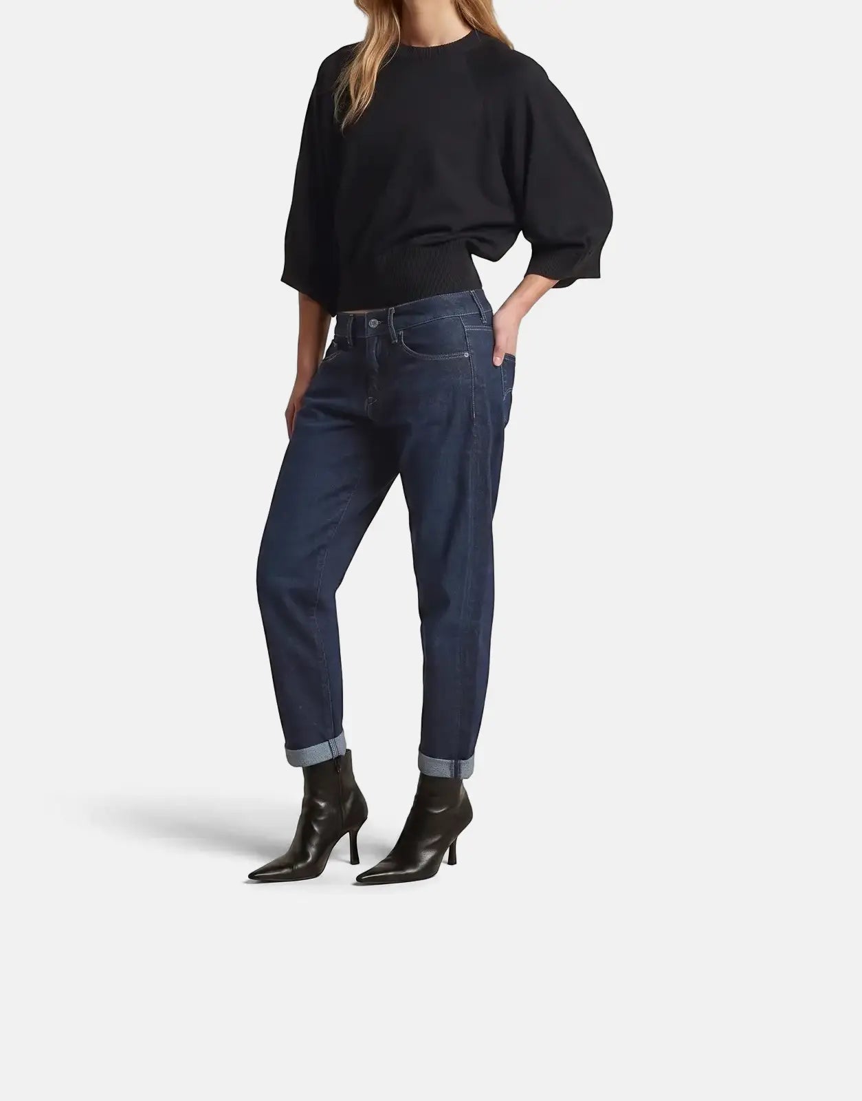 Woman wearing a G-Star RAW Raglan Top in dark black, dark blue cuffed jeans, and black heeled ankle boots, in a full-body