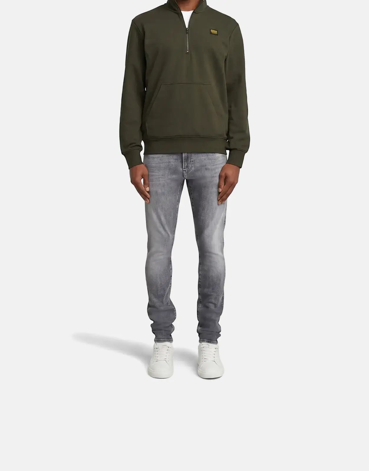 A male model wears G-Star RAW Revend FWD Skinny Faded Shadow Grey jeans, an olive quarter-zip sweatshirt, and white