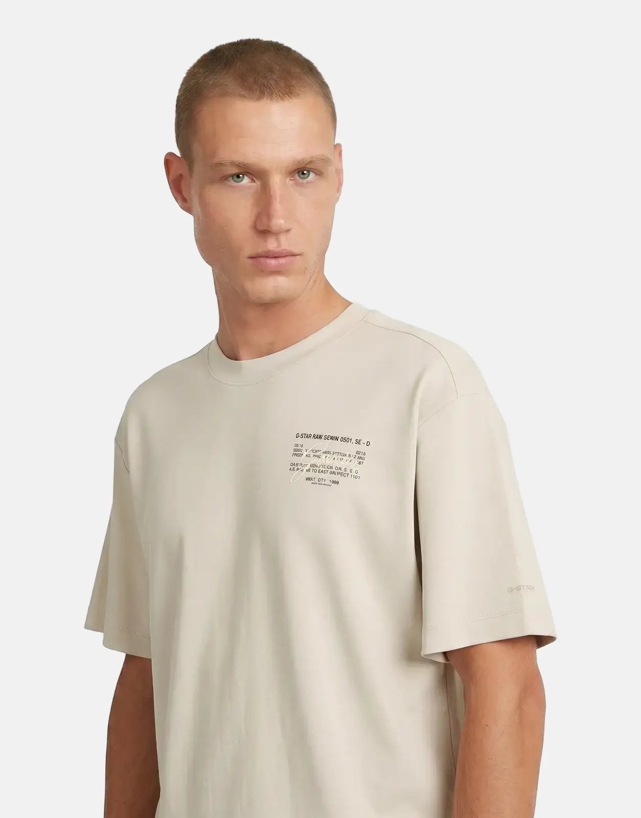 Male model wearing a G-Star RAW Script Whitebait T-Shirt in a light beige, short-sleeved design, shot in a studio.