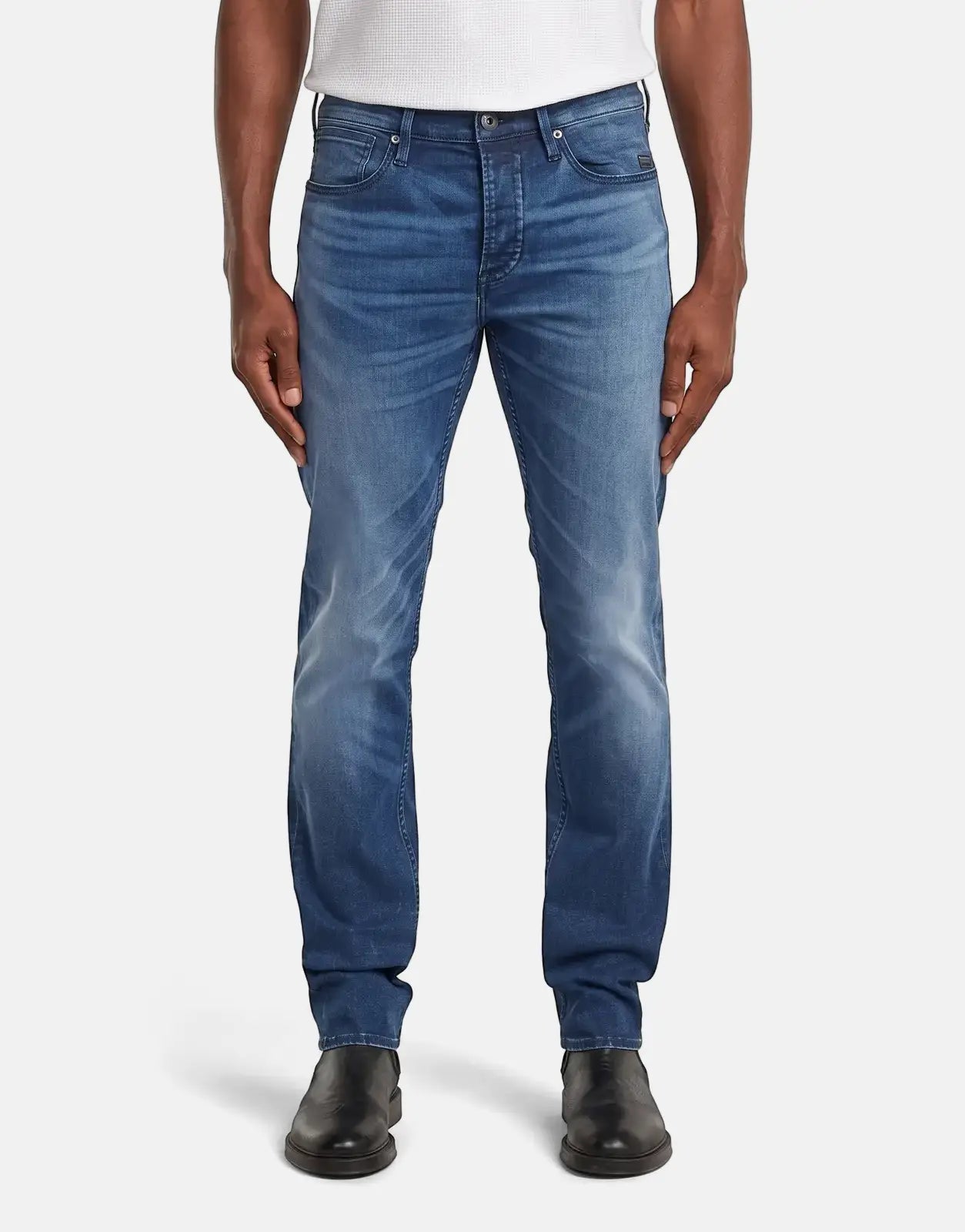 A man models G-Star RAW Streem Slim Tapered jeans in a worn medium blue wash, paired with black shoes, full length view.