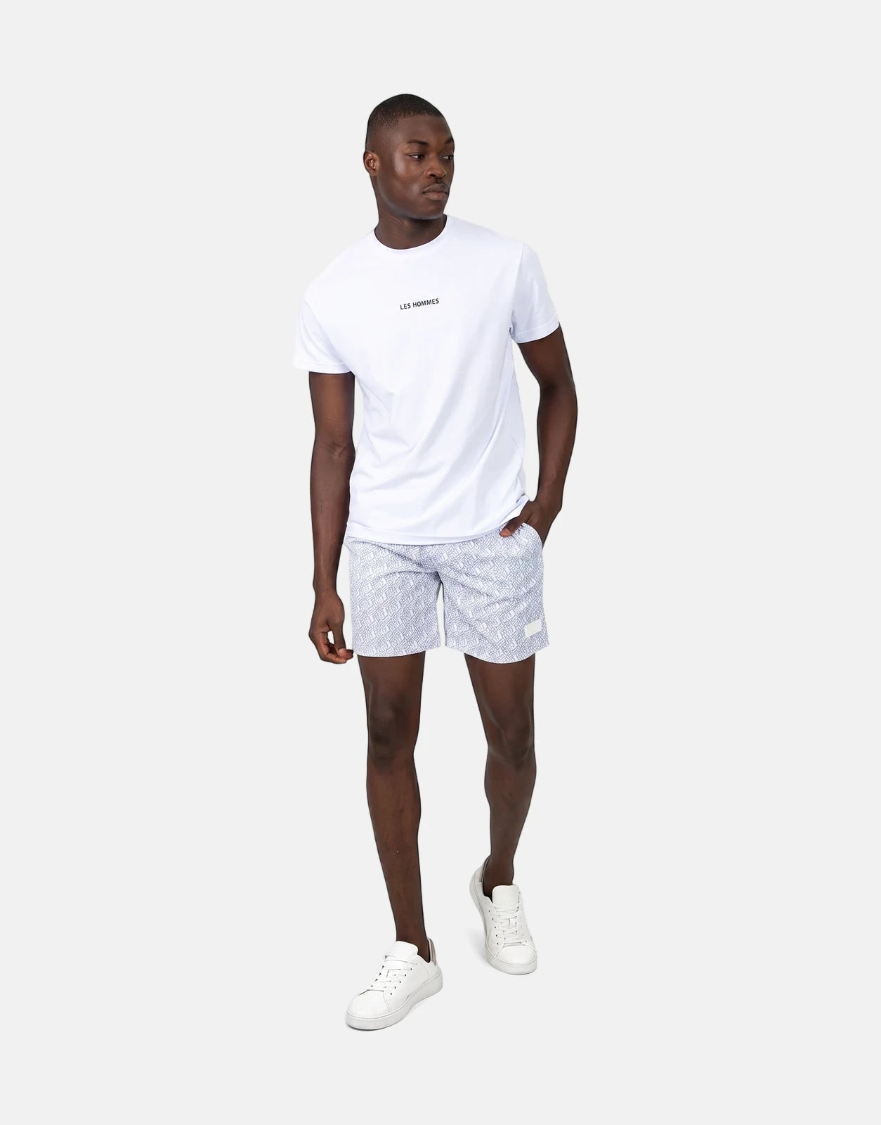 Male model wearing Les Hommes AOP white swim shorts with a geometric pattern and a white t-shirt, standing.