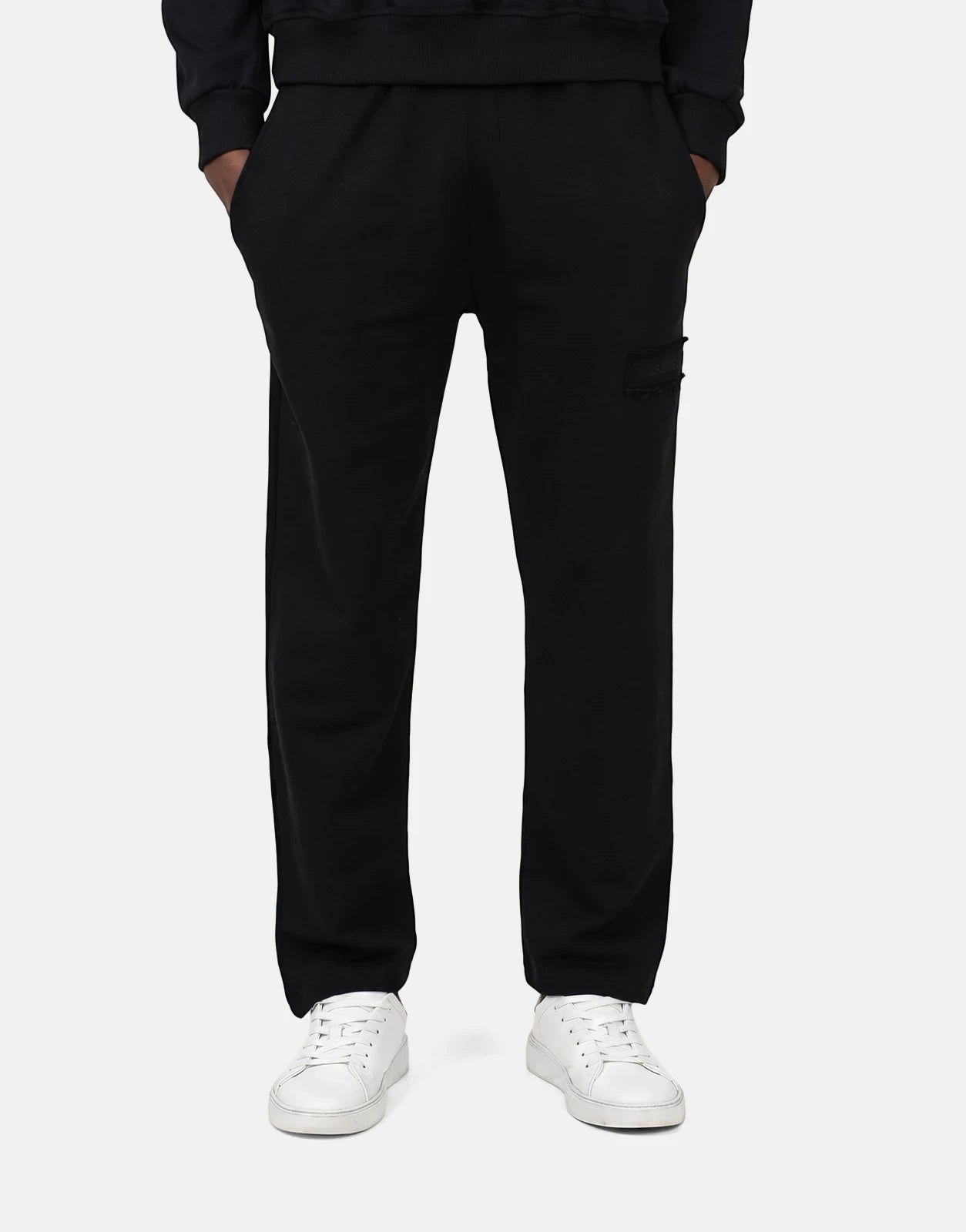 Les Hommes Black Jogger worn by a person, featuring a comfortable fit and white sneakers. Front view.