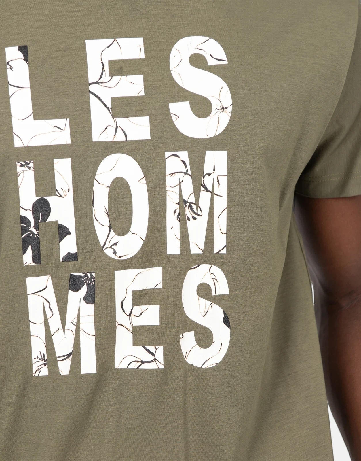 Close-up of an olive green Les Hommes t-shirt featuring a unique white chest graphic with black floral patterns, worn by a