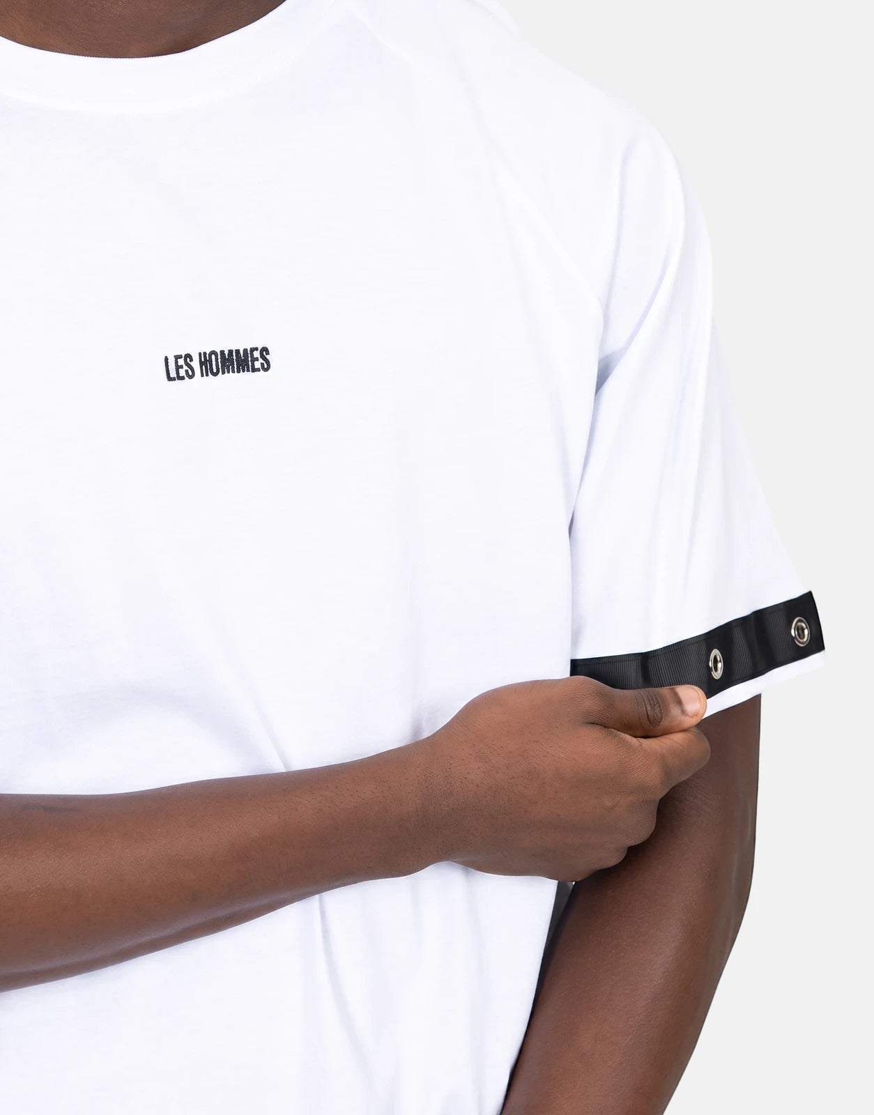 Close-up of a model wearing a Les Hommes white t-shirt with black eyelet sleeve detail and brand logo.