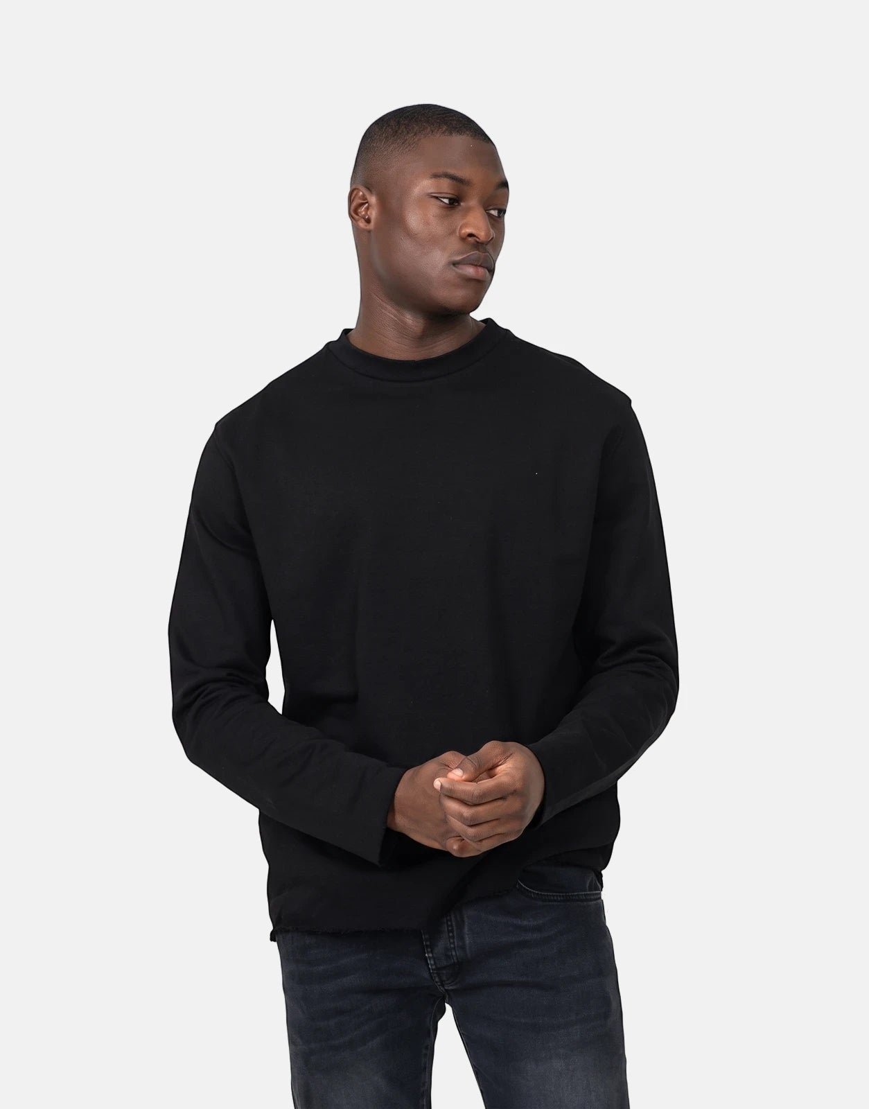 A male model wears a black Les Hommes Dragonfly crew-neck long-sleeve sweatshirt with dark jeans, posed against a white