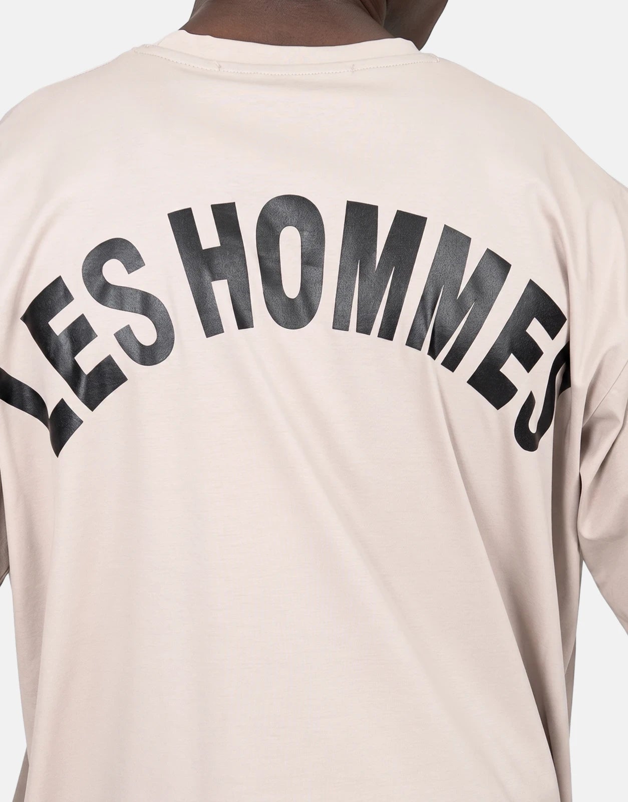 Back view of a Les Hommes oversized t-shirt in light beige, featuring a large arched black logo print on the back.
