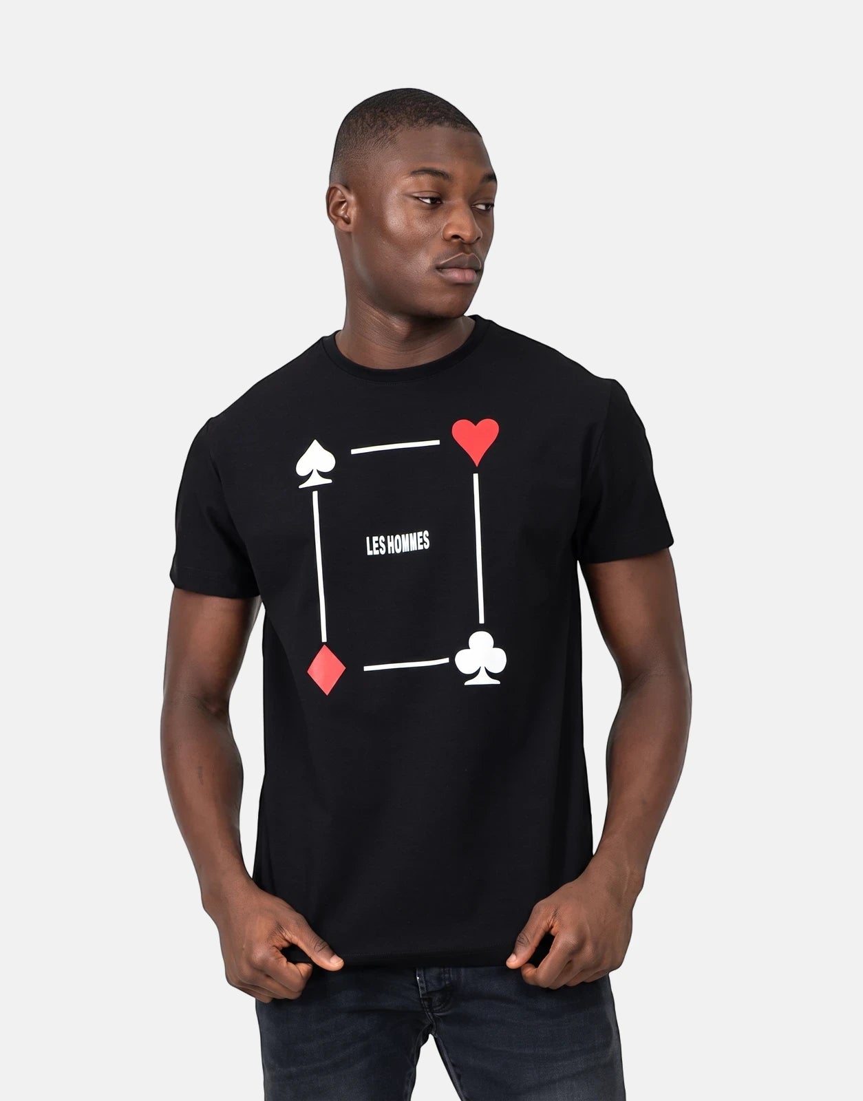 A Black male model wears a black Les Hommes Poker Print T-shirt with red heart and diamond symbols and white spade and club