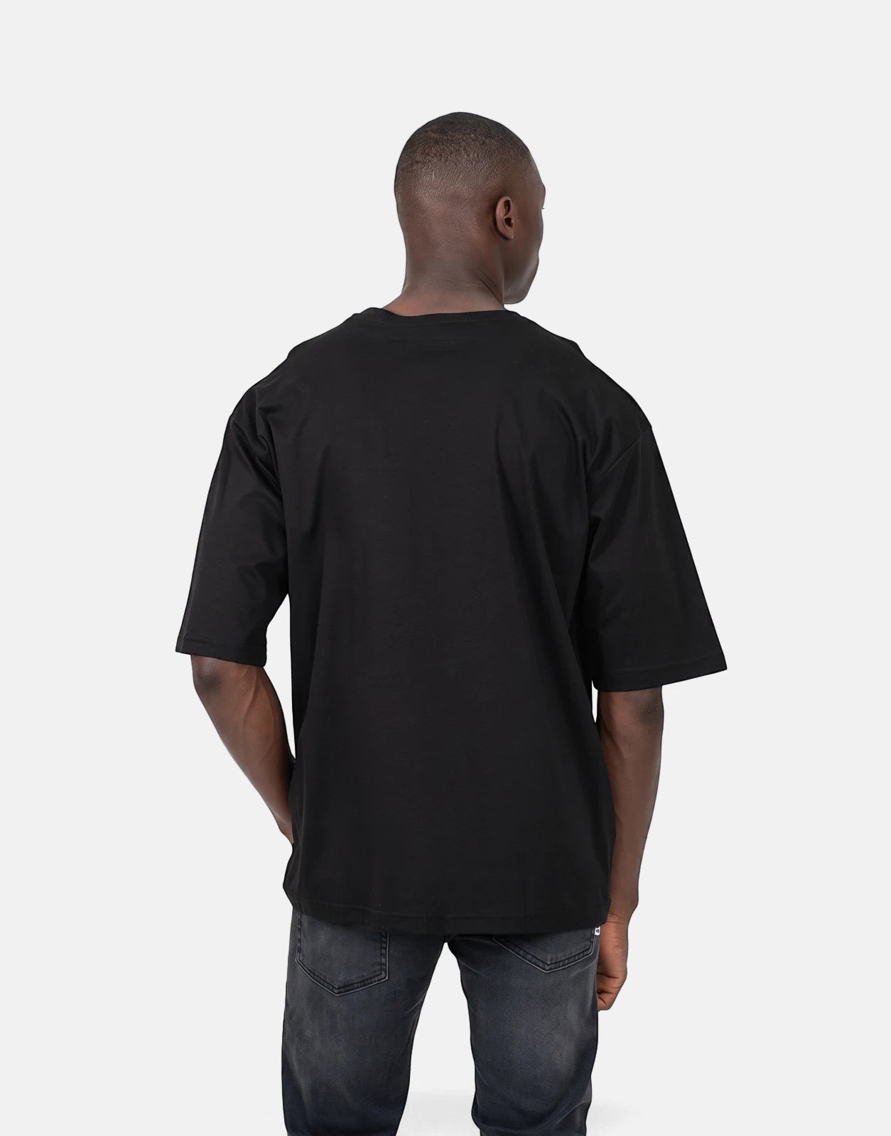 Back view of a Black Les Hommes Queen King T-Shirt with an oversized fit, worn by a male model and paired with dark jeans.