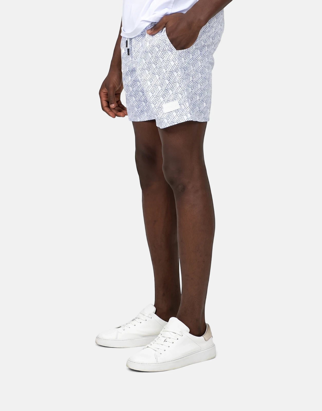 Men's Less Hommes AOP white swim shorts with a geometric pattern, worn by a model and paired with white sneakers.
