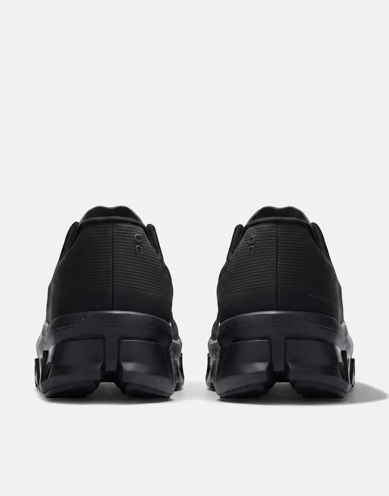 Rear view of two On Men's Cloudmonster Void Black Sneakers, showcasing their black textured design and chunky soles.