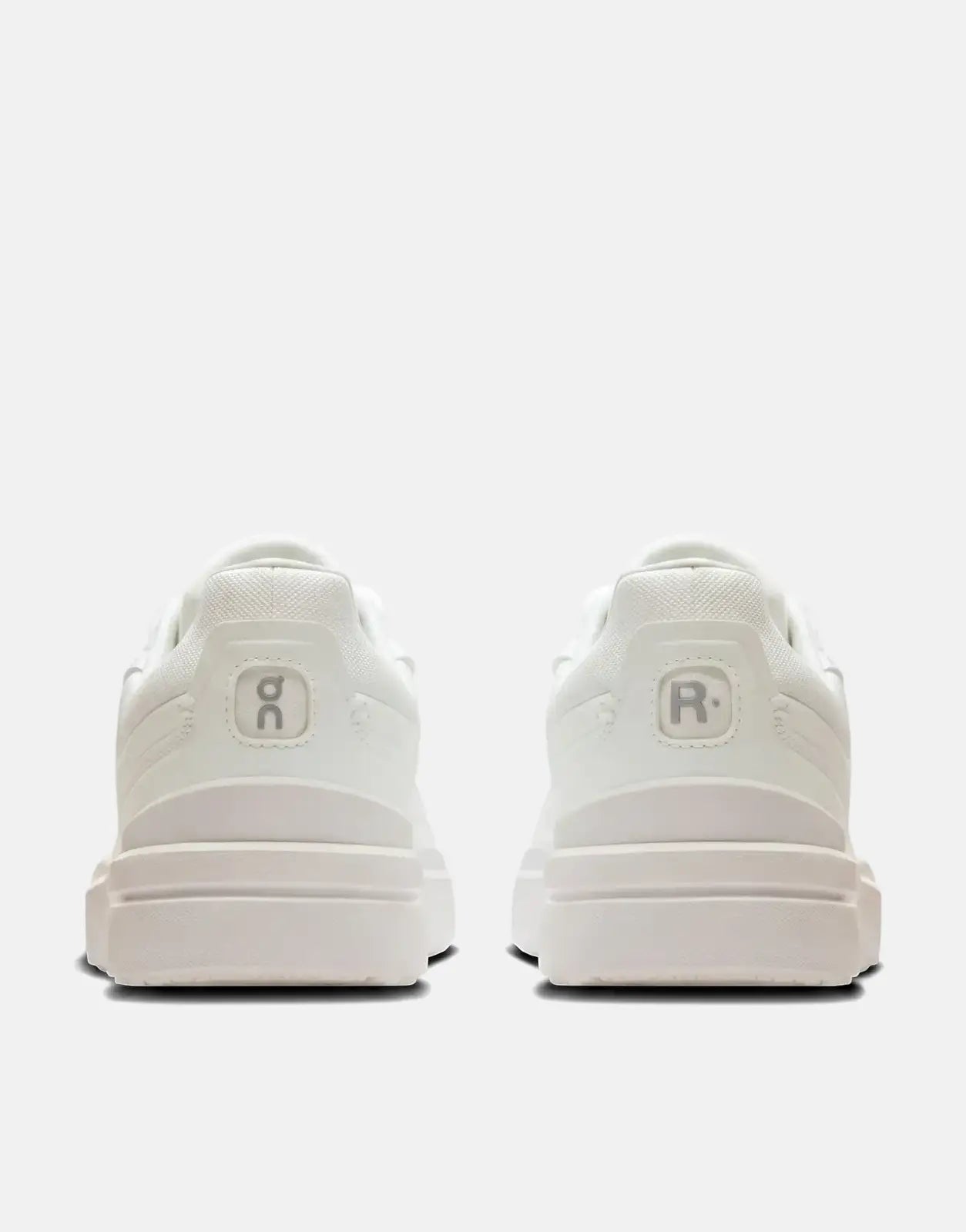 Rear view of two On Men's Roger Advantage white sneakers, showing the heel designs with the On logo and R logo.