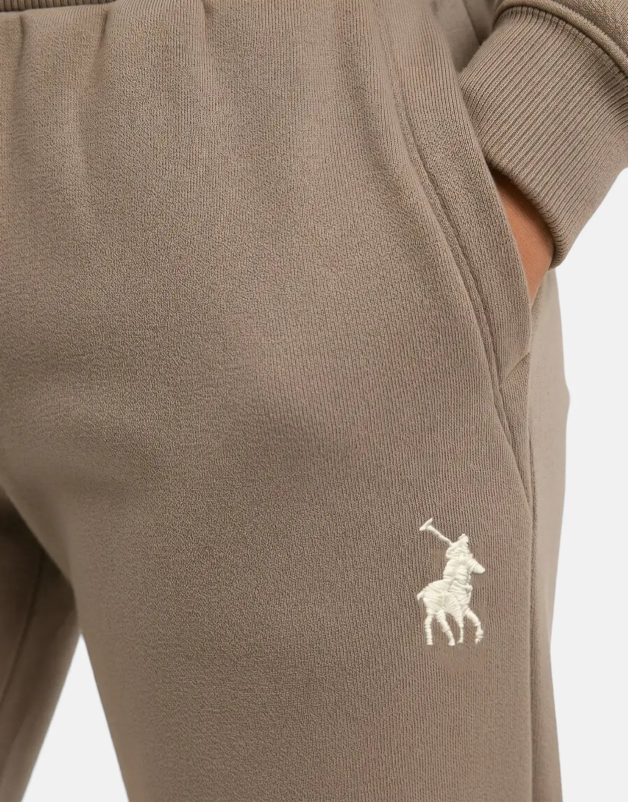 Close-up of brown Polo Girls Kim Pull On Iron Jogger, featuring an embroidered logo and a visible pocket with a hand inside.