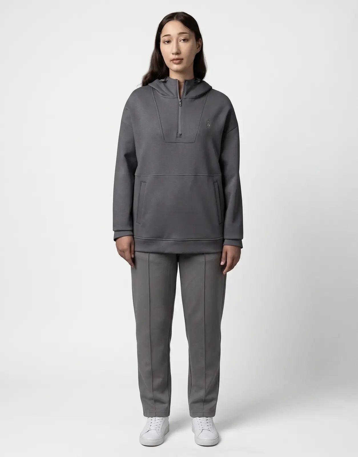 A woman wears a dark grey Polo Robyn LS Gunmetal Track Top, featuring a half-zip design, long sleeves, and a hood, viewed