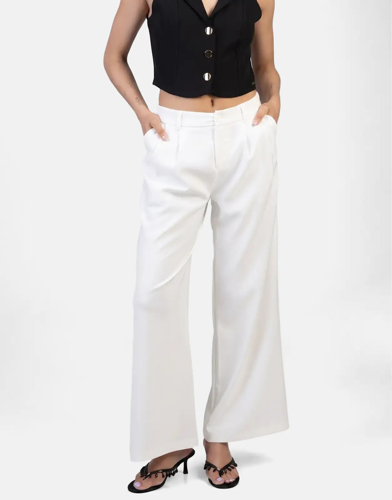 Model wearing Sissy Boy Alice wide leg off-white trousers, paired with a black sleeveless top and black embellished sandals.