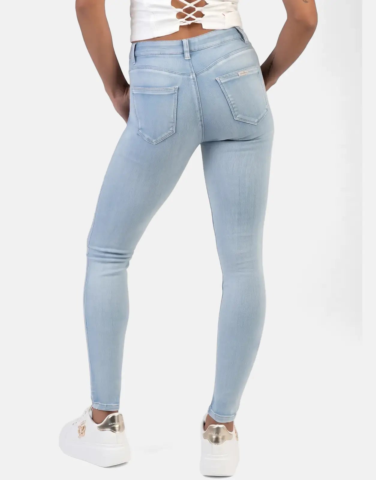 Rear view of a model wearing Sissy Boy Cara Light Vintage Mid Waist Skinny Jeans, paired with a white top and sneakers.
