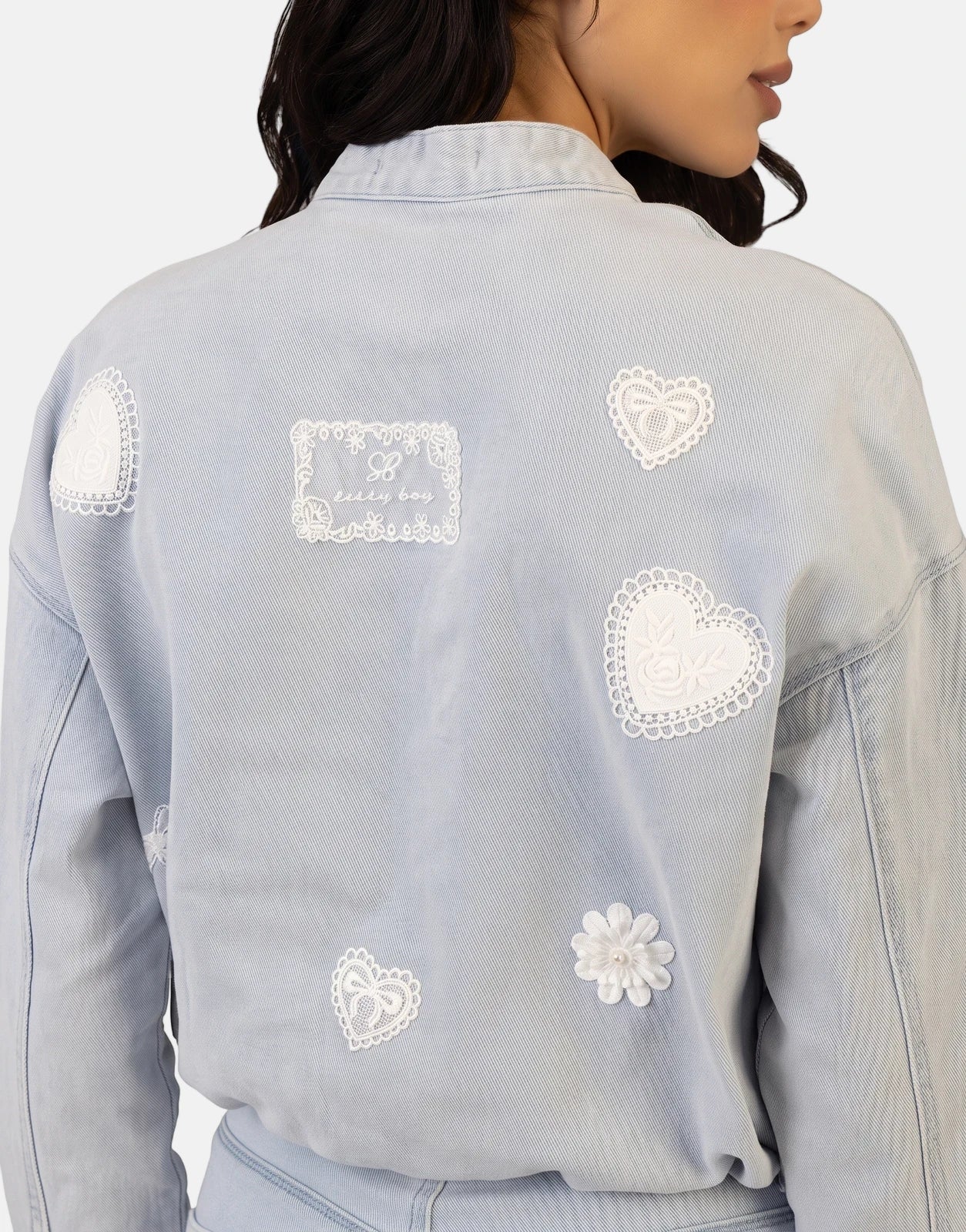 Sissy Boy Kiera Light Vintage Denim Bomber Jacket for women, featuring intricate white lace heart and flower patches on the