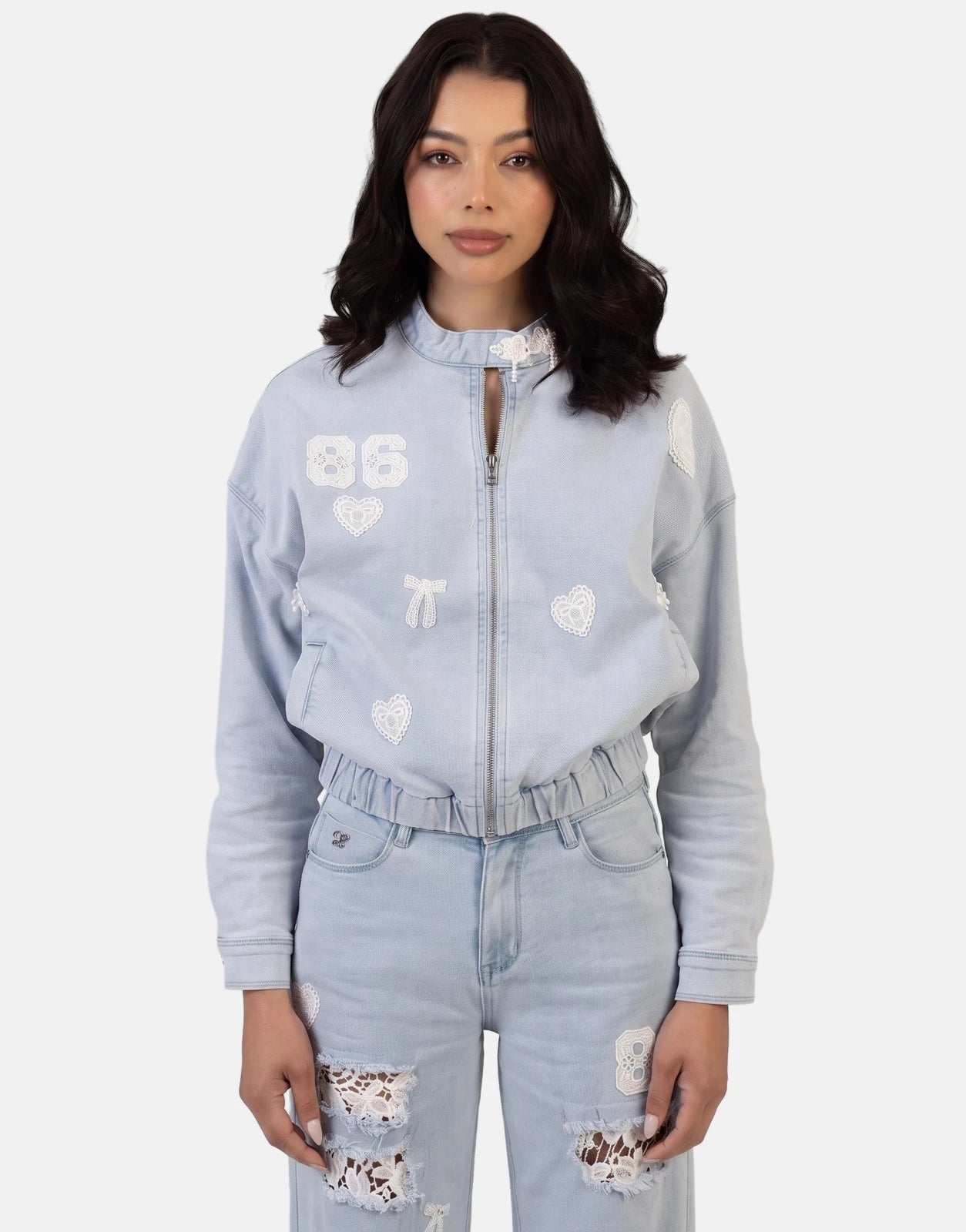 Front view of a woman wearing a Sissy Boy Kiera Light Vintage Denim Bomber Jacket and matching jeans with white lace patches.