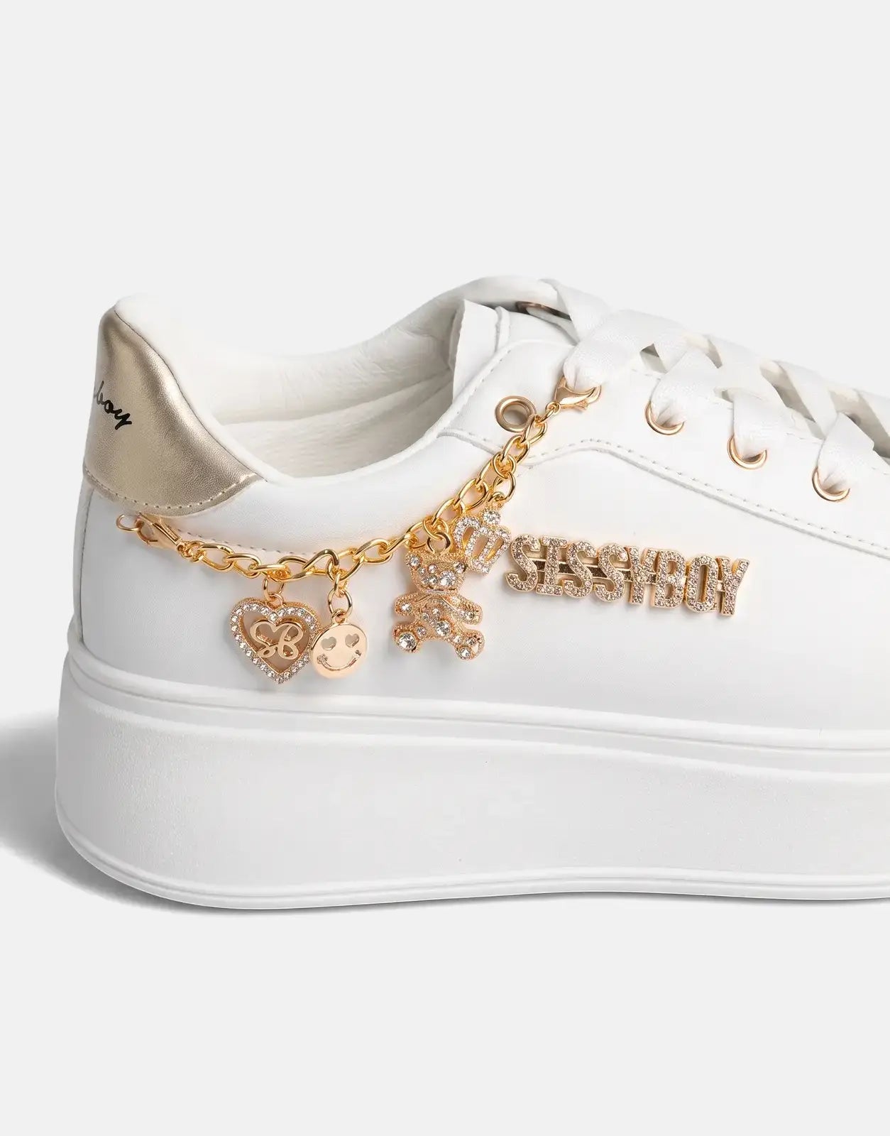 Close-up side view of Sissy Boy Tatum white and gold platform sneakers, featuring a decorative gold chain with various