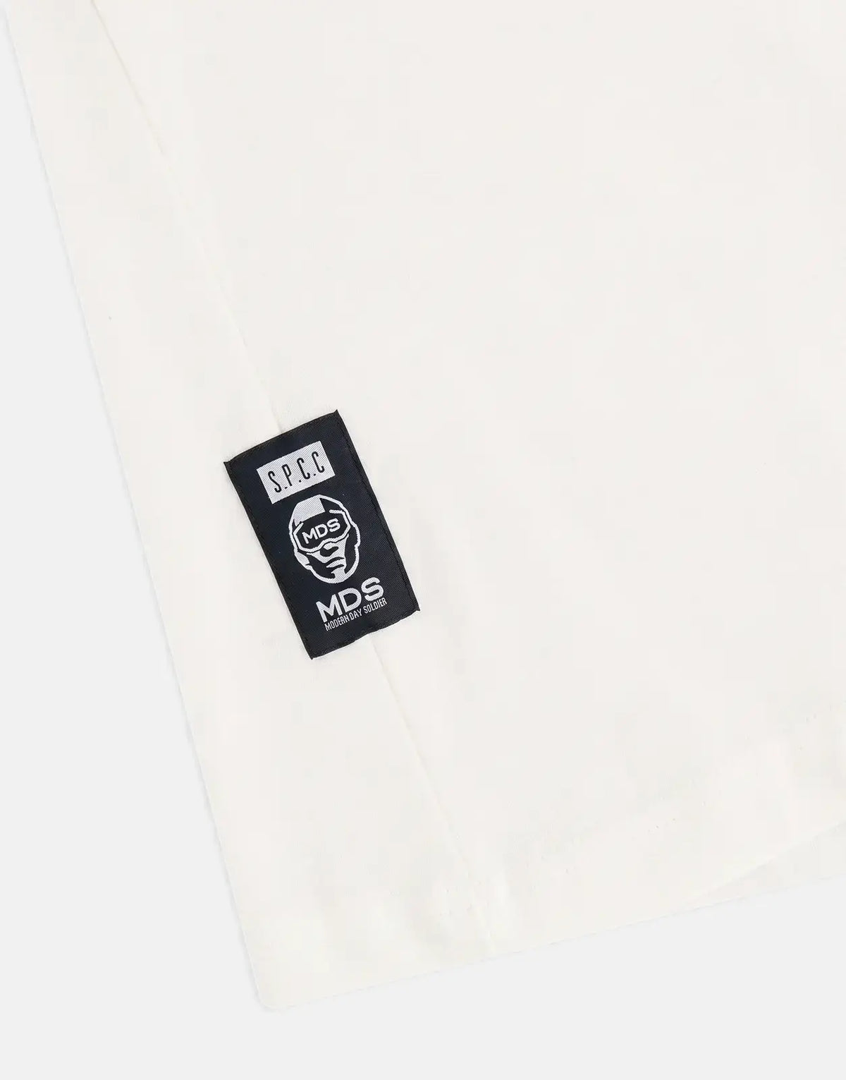 Close-up of an SPCC MDS Axel off-white t-shirt featuring a black woven label with a skull graphic and text.