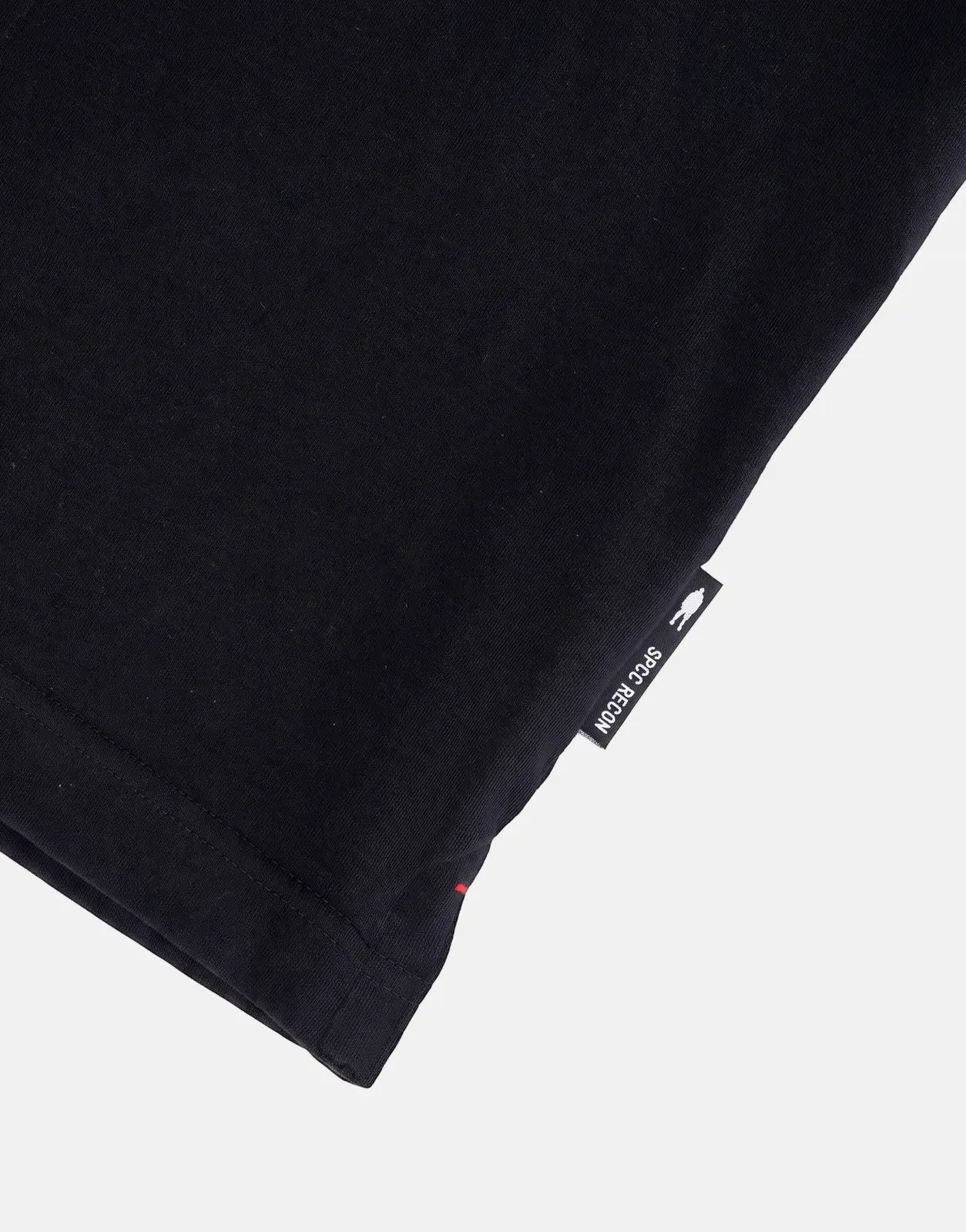 Close-up view of the hem and woven label on a black SPCC Recon Overwatch T-shirt, showing the brand logo.