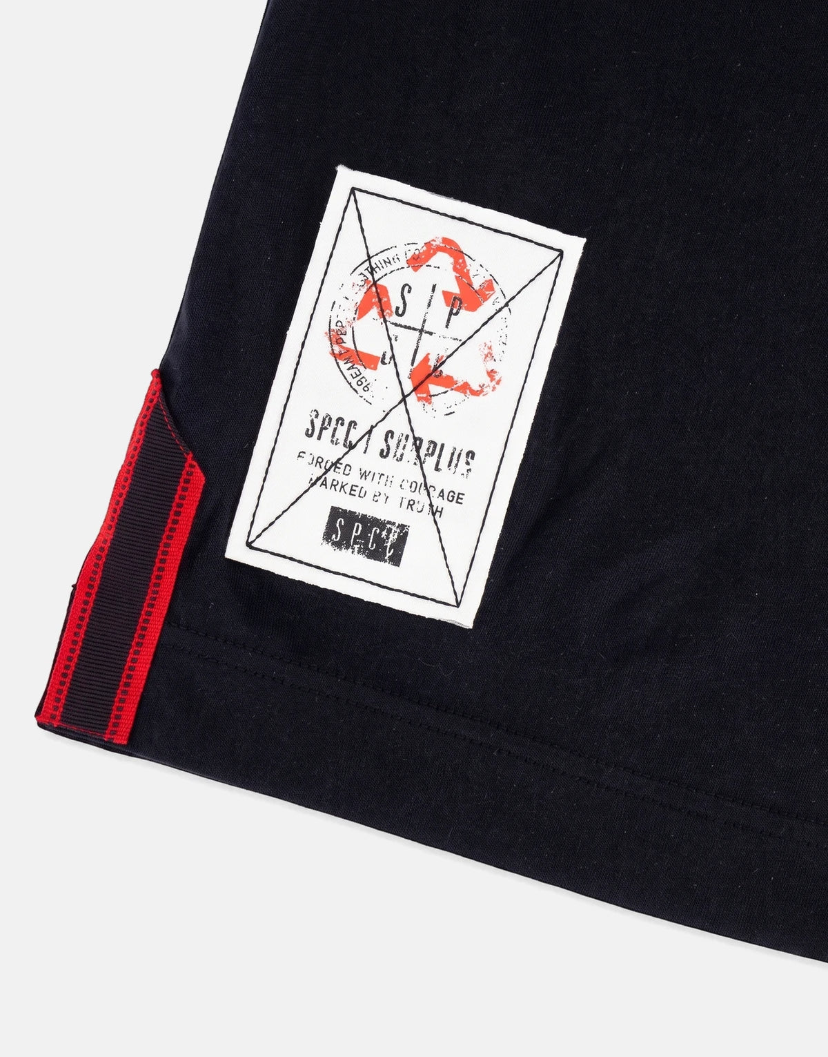 Close-up of a black SPCC Roarke Golfer shirt featuring a white fabric label with distressed branding and a red and black