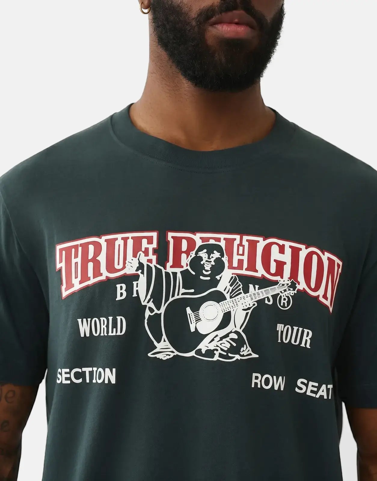 A man wearing a dark green True Religion Buddha Arch Logo T-Shirt, featuring red arched text and a white Buddha graphic