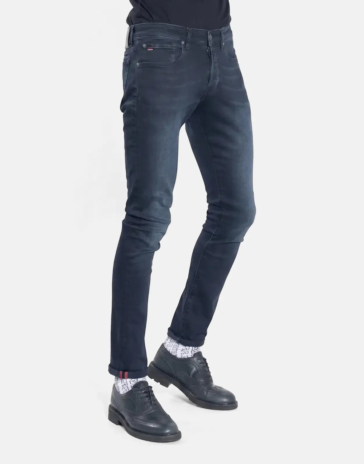 TSHEPO Takalani Jeans, dark wash men's slim fit denim with cuffed hem, worn with patterned socks and black brogue shoes.