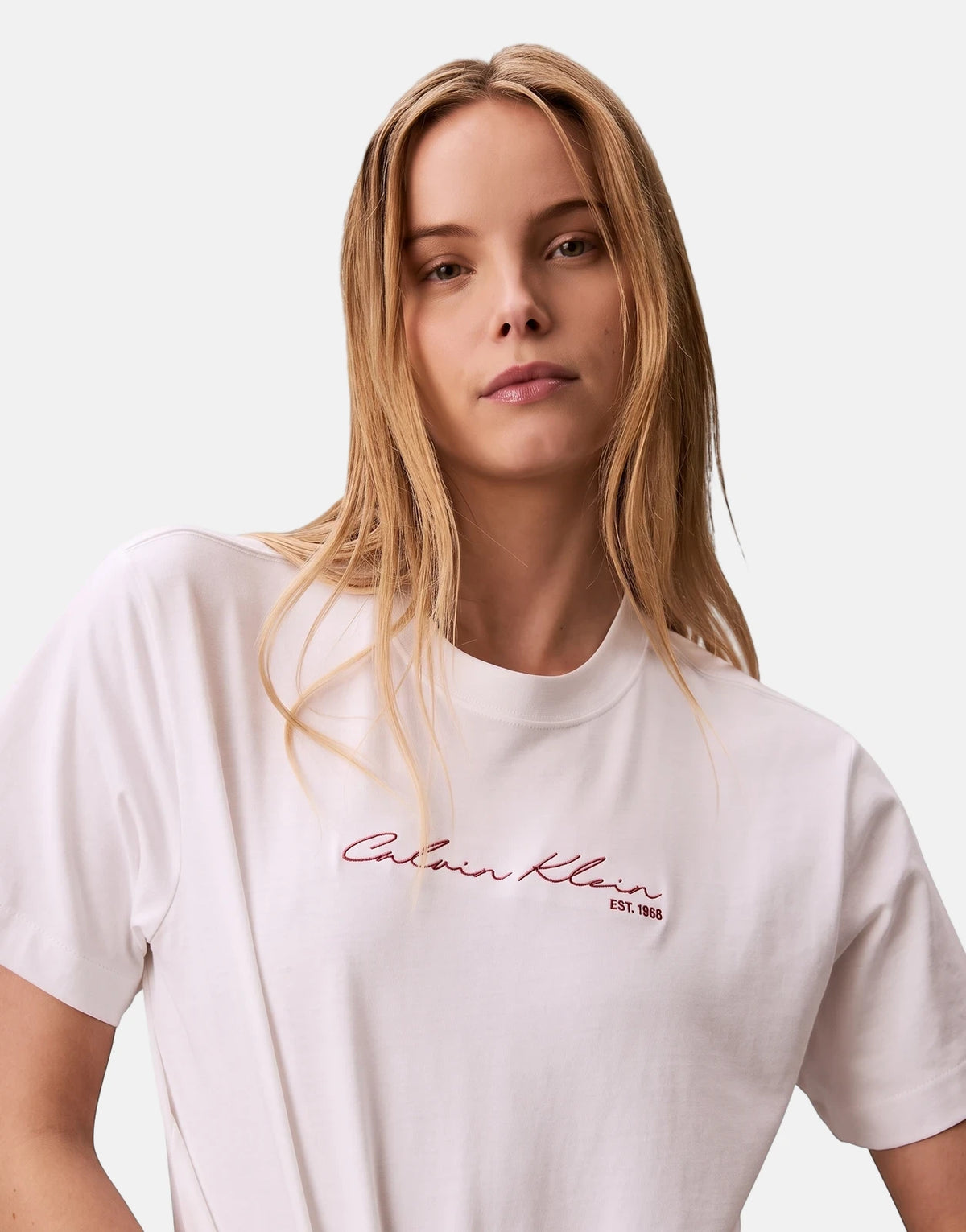 Woman in white Calvin Klein Graphic Boxy T-Shirt with red embroidered logo, standing waist-up